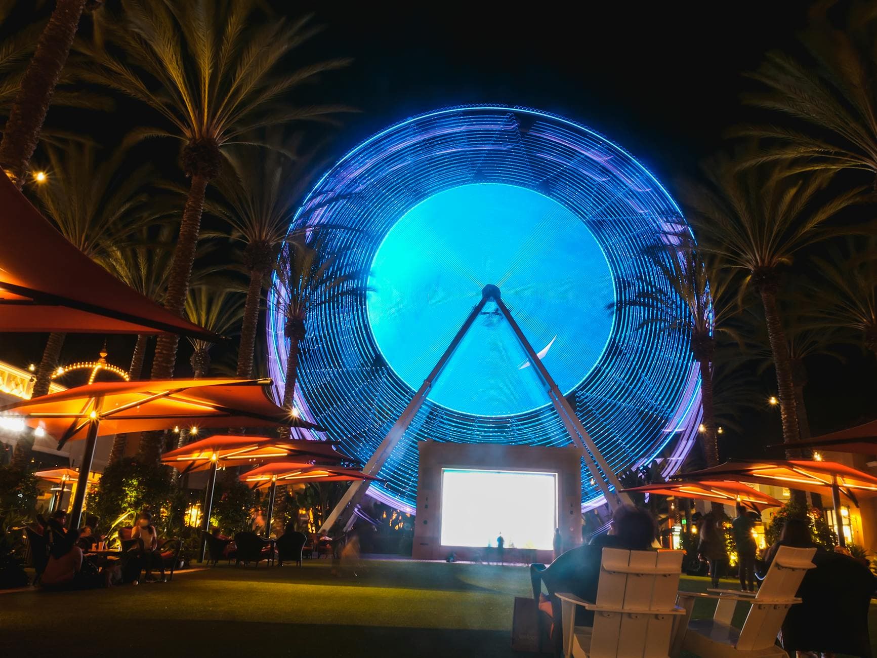 Night view of a brightly lit Ferris wheel surrounded by tropical trees at Irvine Spectrum Center.