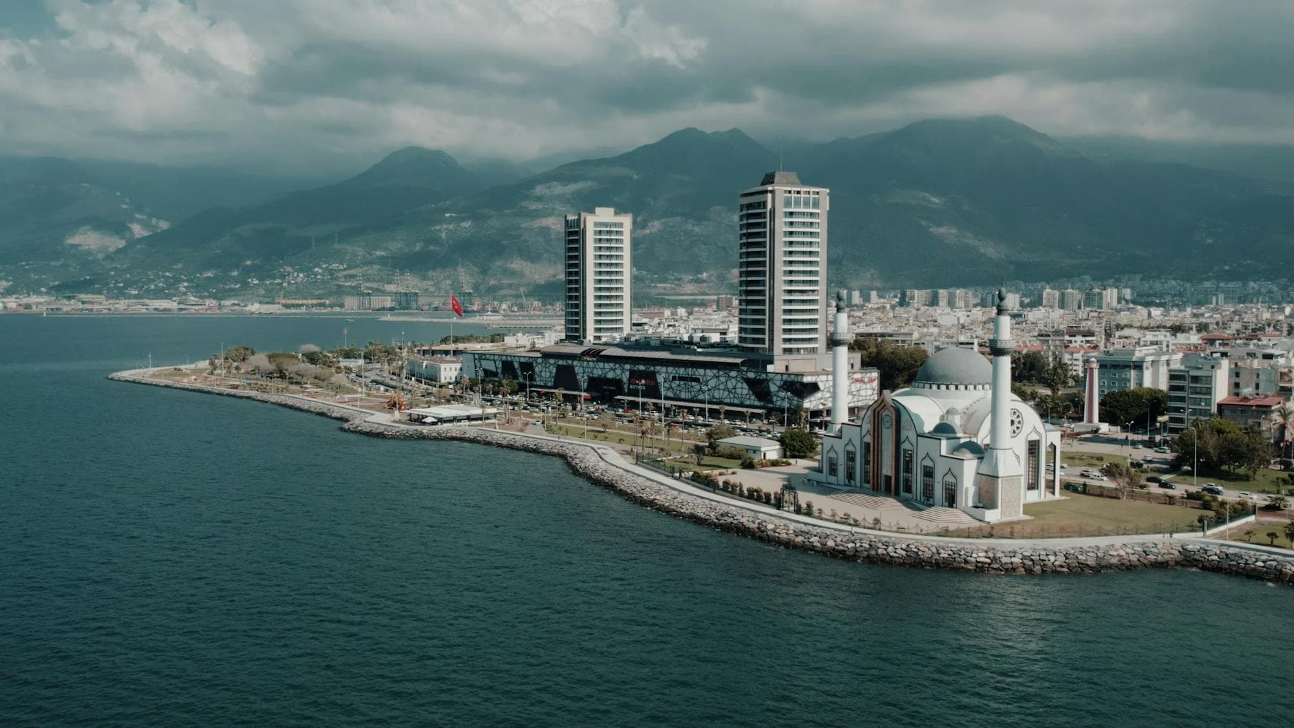 A stunning aerial shot of İskenderun, Turkey, featuring a mosque, coastline, and modern architecture.