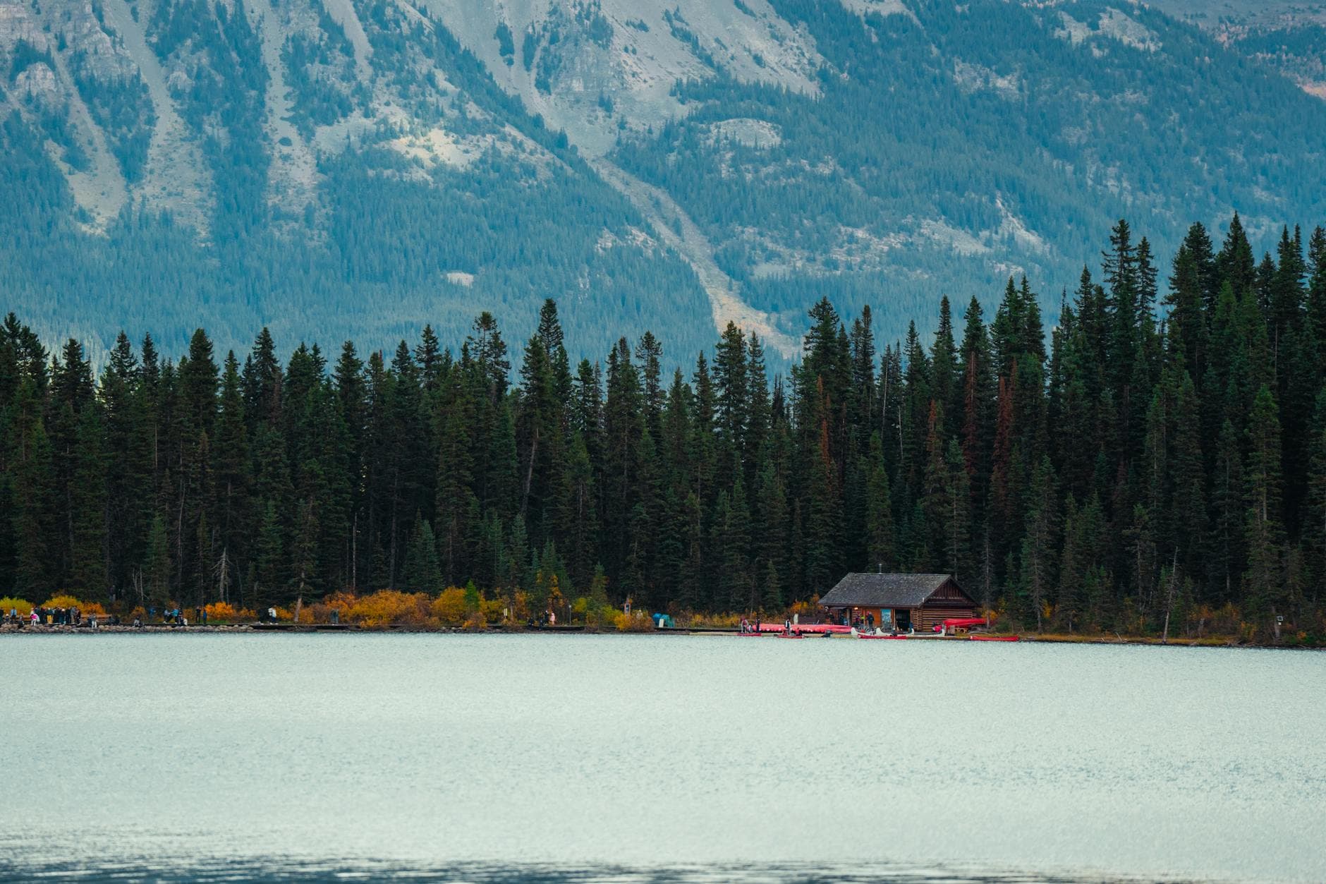 Peaceful lake view with forested shore, cabin and mountain backdrop.