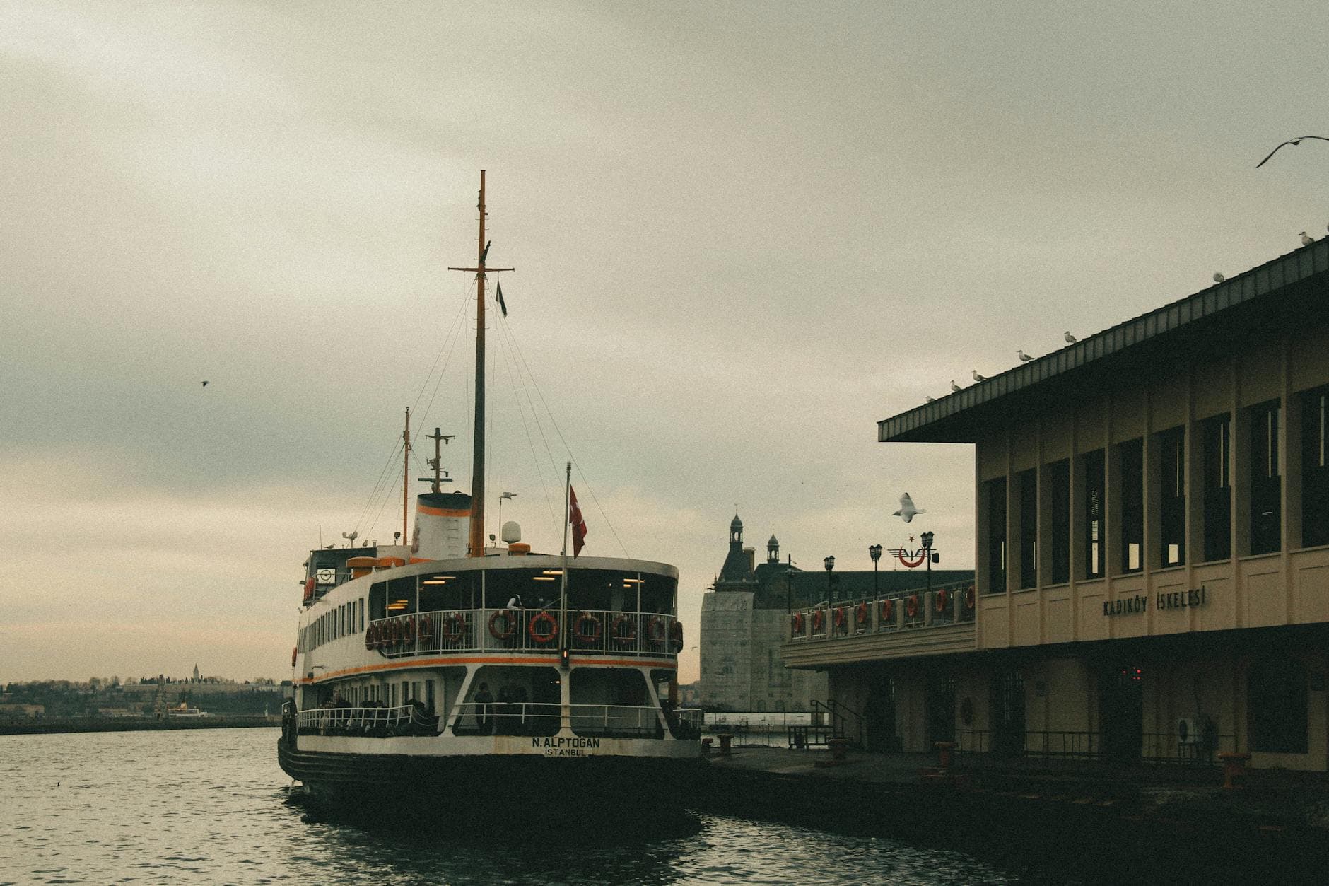 Ferry docked at Kadıköy pier, with Istanbul skyline and sea in view.