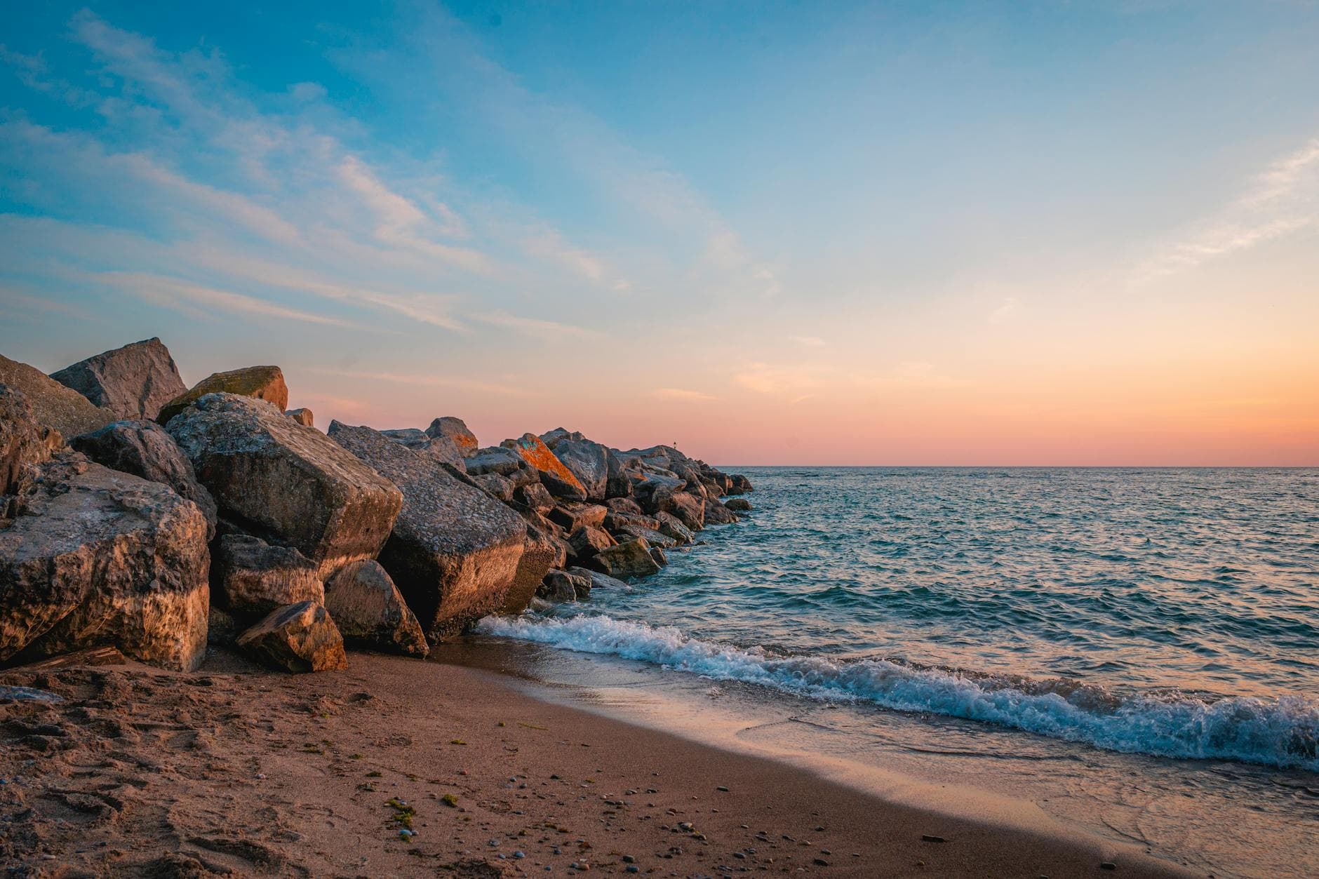 A serene sunset view over the rocky beach in Toronto, Canada. Waves gently crash against the shore.