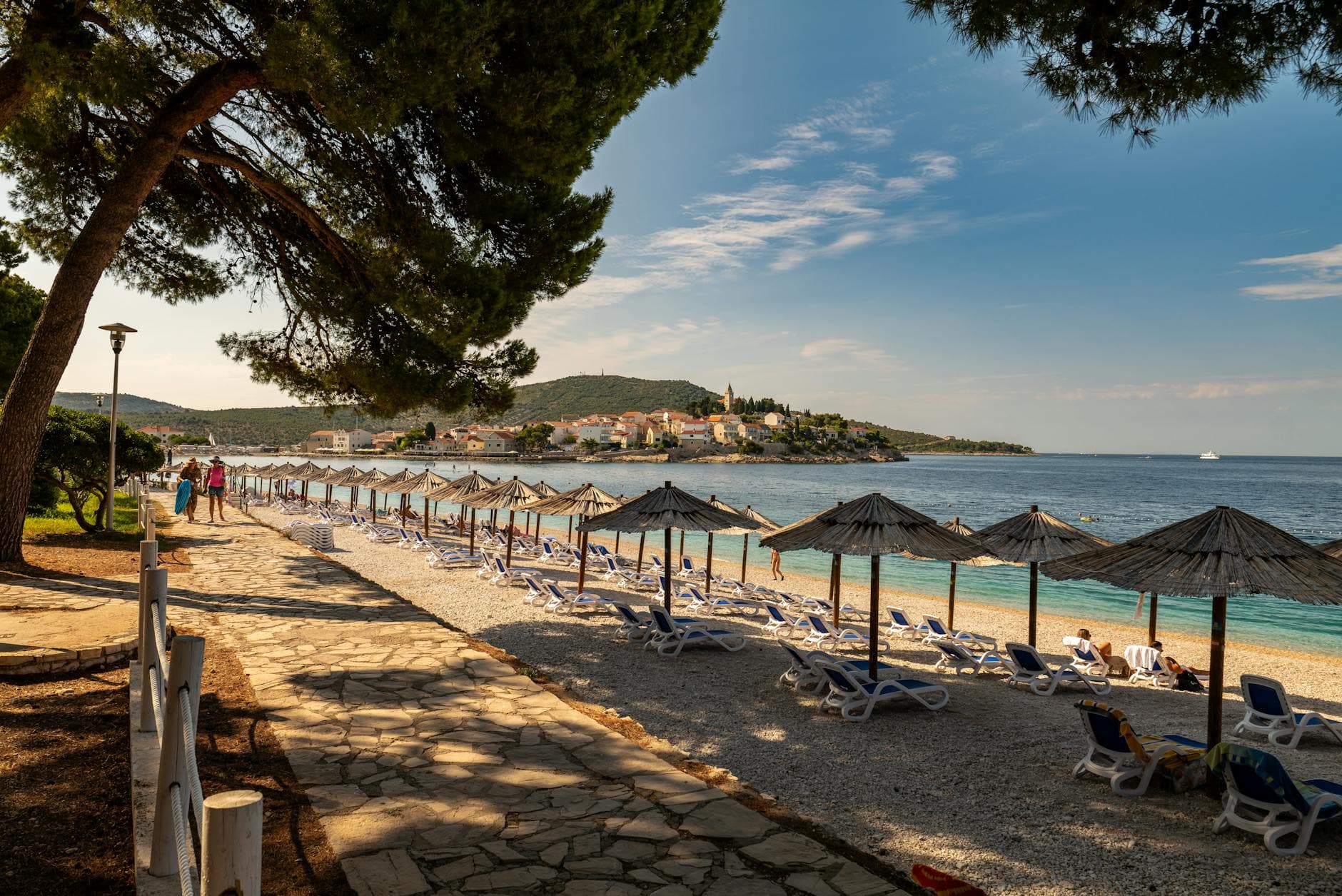 Beautiful coastal scenery with beach umbrellas and town view in Primošten, Croatia.