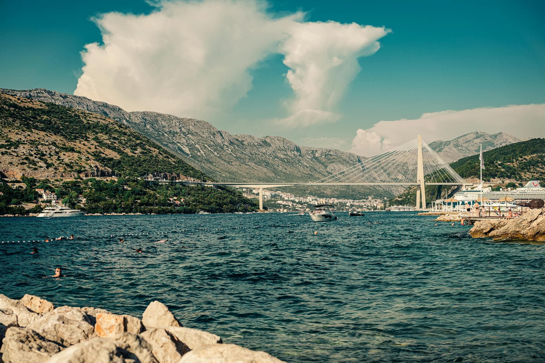 Picturesque seascape of Franjo Tuđman Bridge in Dubrovnik with swimmers enjoying a sunny day.