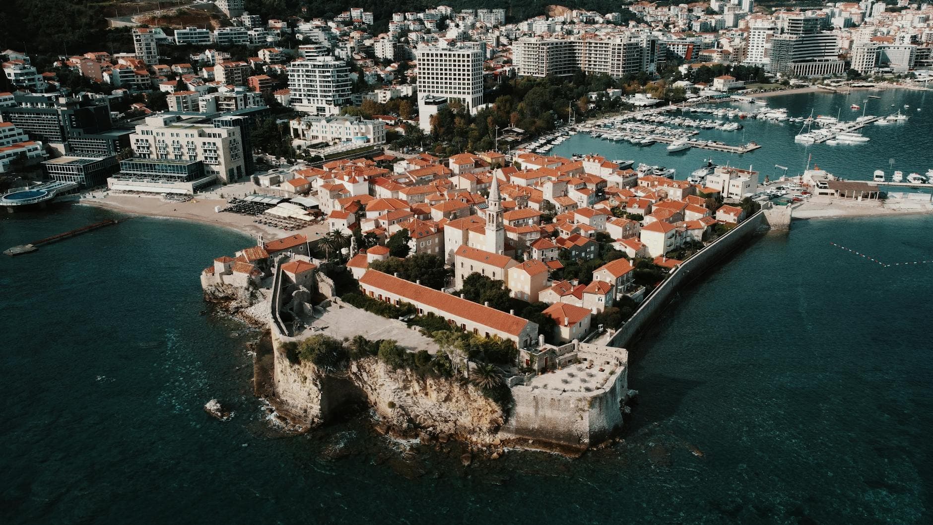 Aerial view of Budva's picturesque old town with red tile roofs, citadel, and seaside harbor.