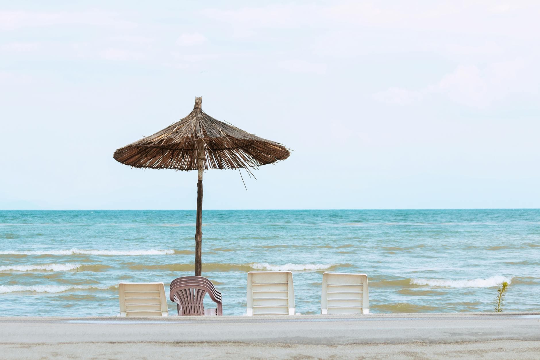 Peaceful view of a beach with a straw umbrella and chairs in Pogradec, Albania.