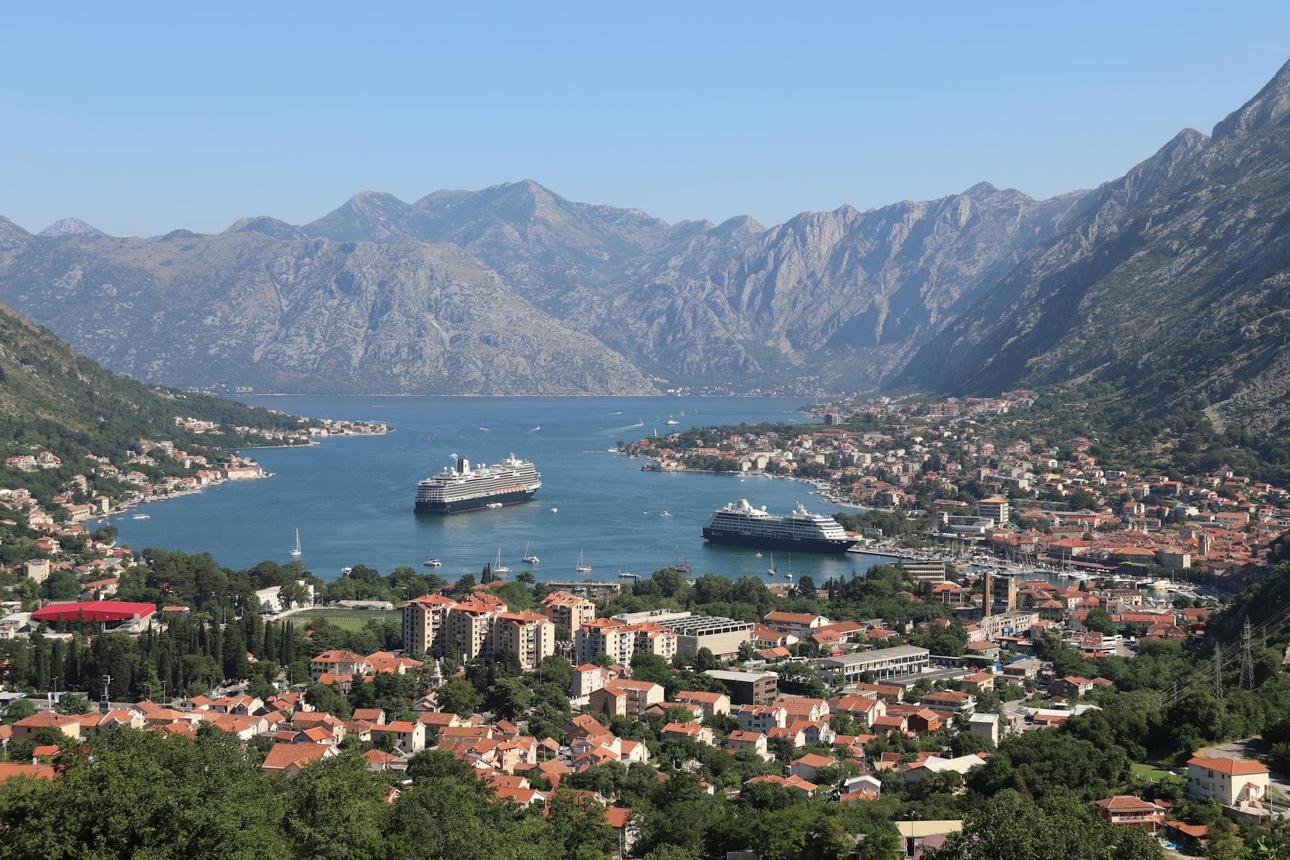 Scenic panorama of Kotor Bay with cruise ships and historic town surrounded by mountains.