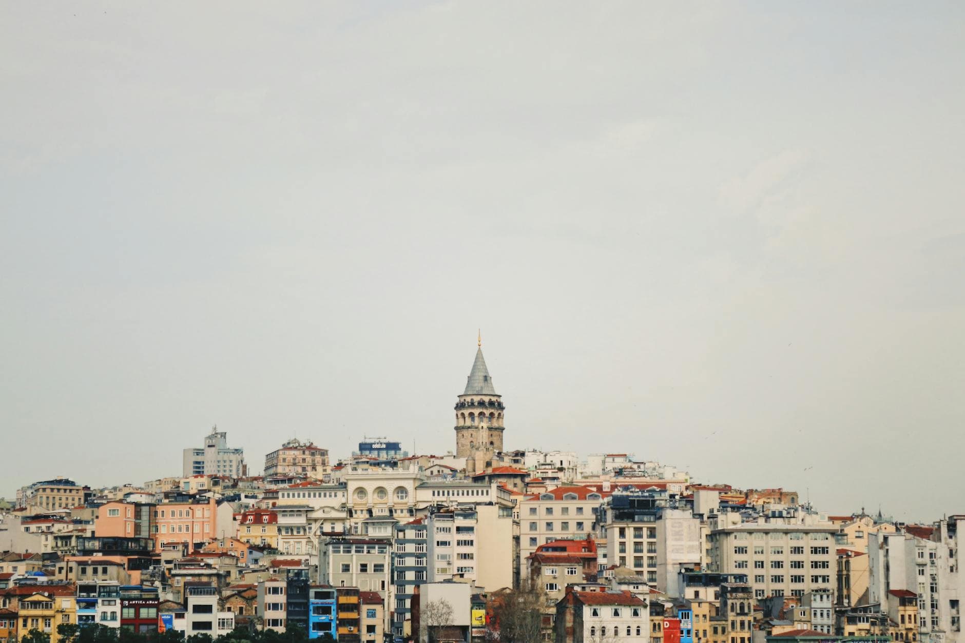 Scenic view of Istanbul's Galata Tower amidst a bustling cityscape, under a cloudy sky.