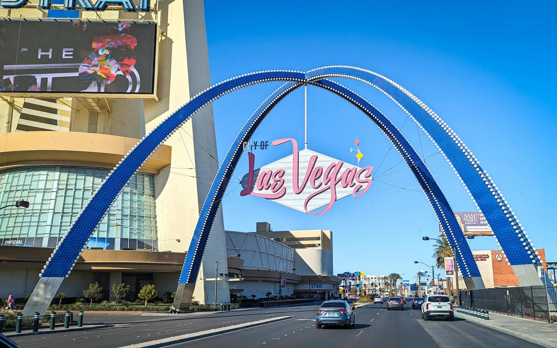 View of the modern Las Vegas arch over a busy street with urban buildings.