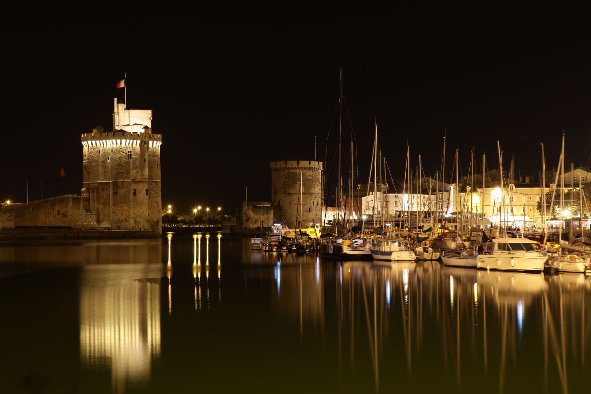 Scenic night photograph of La Rochelle harbor with illuminated historic towers reflecting on the water.