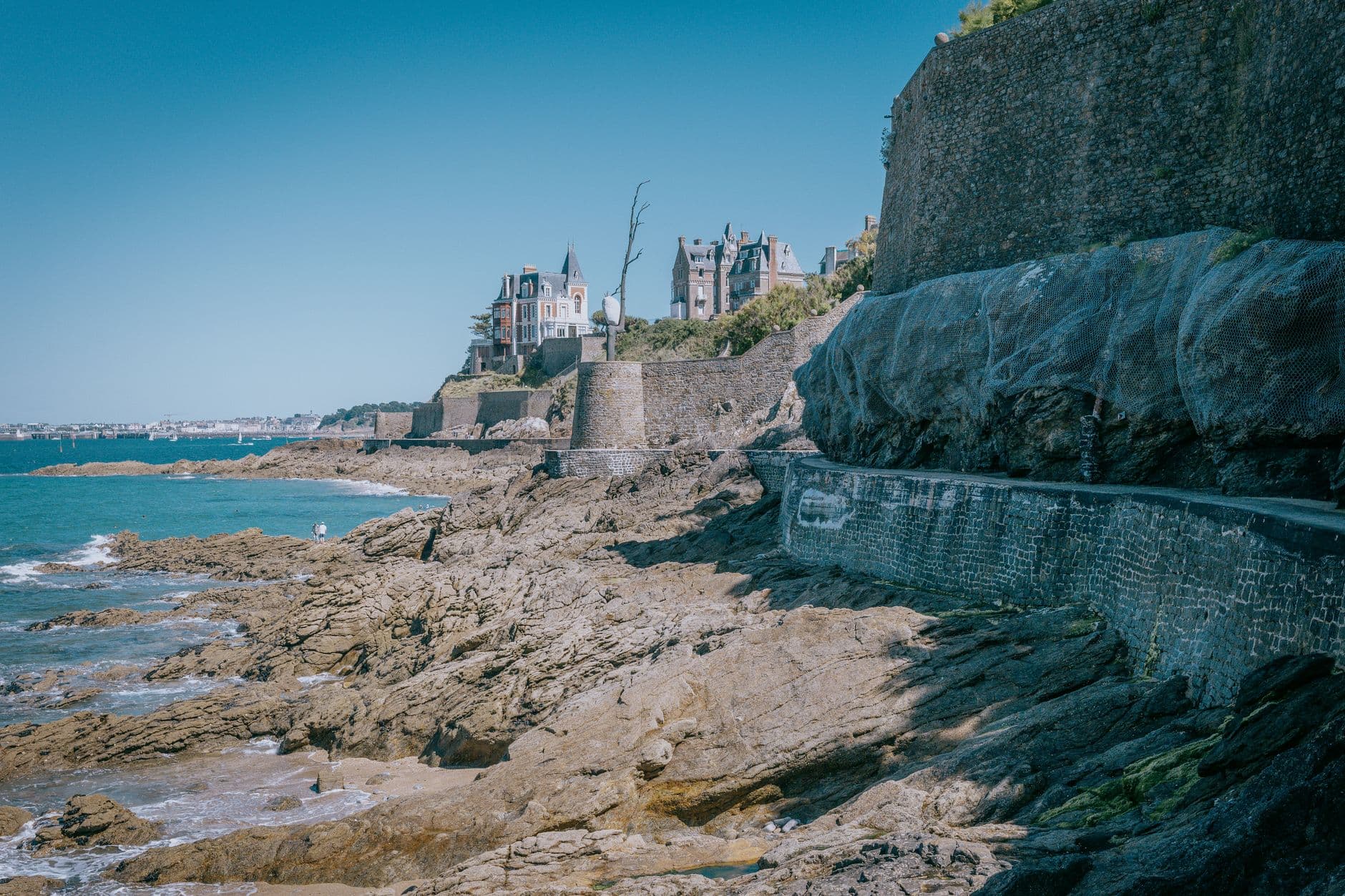 Explore the stunning rocky coastline and historic architecture of Dinard, France, under clear summer skies.