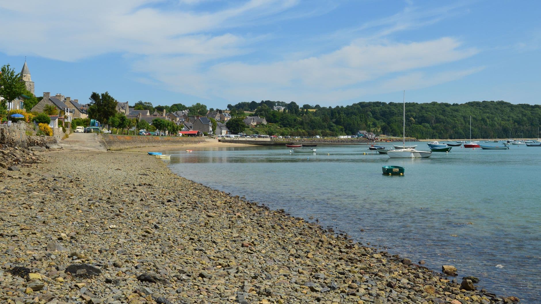 Charming coastal village of Saint-Suliac with boats and pebbled shore under a blue sky.