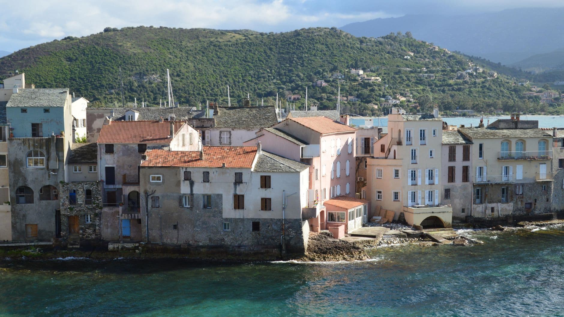 Picturesque view of Saint-Florent's seaside village with colorful buildings and stunning landscape in Corsica, France.