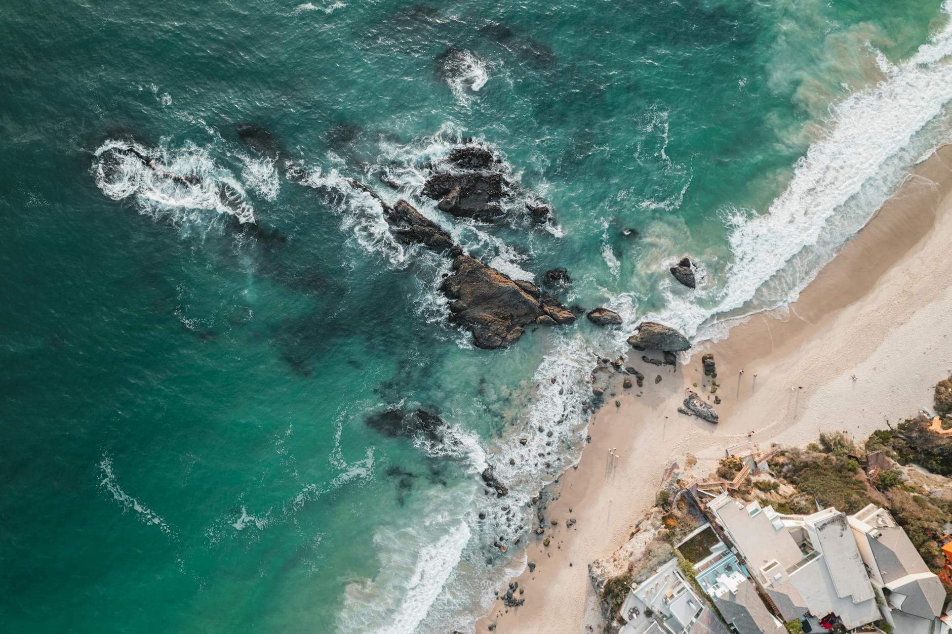 A stunning aerial view of Laguna Beach, showcasing waves, rocks, and coastal buildings.