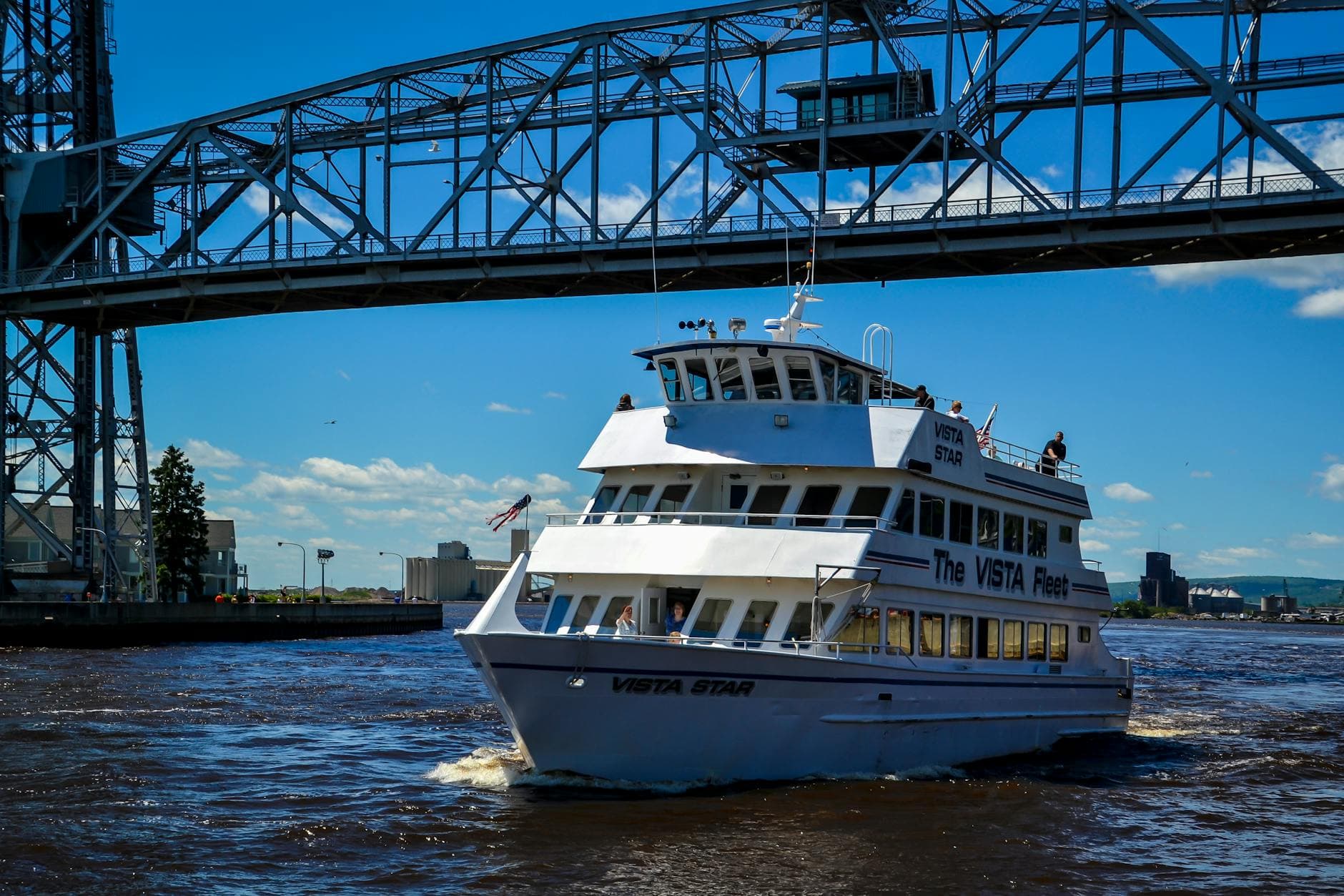 A Vista Fleet boat cruises under Duluth's iconic Aerial Lift Bridge on a sunny day.