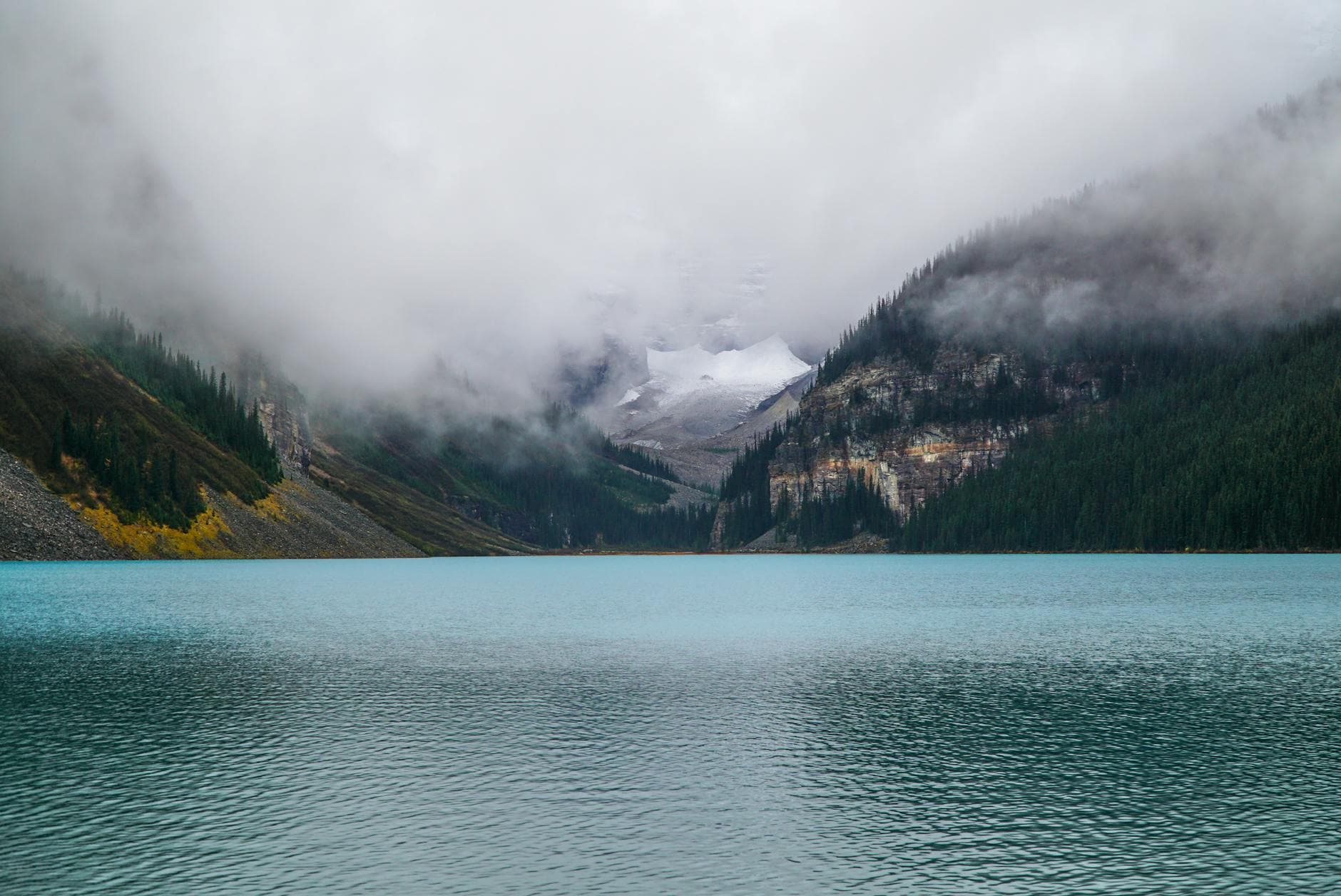 Scenic view of foggy Lake Louise surrounded by mountains in Banff, Canada.