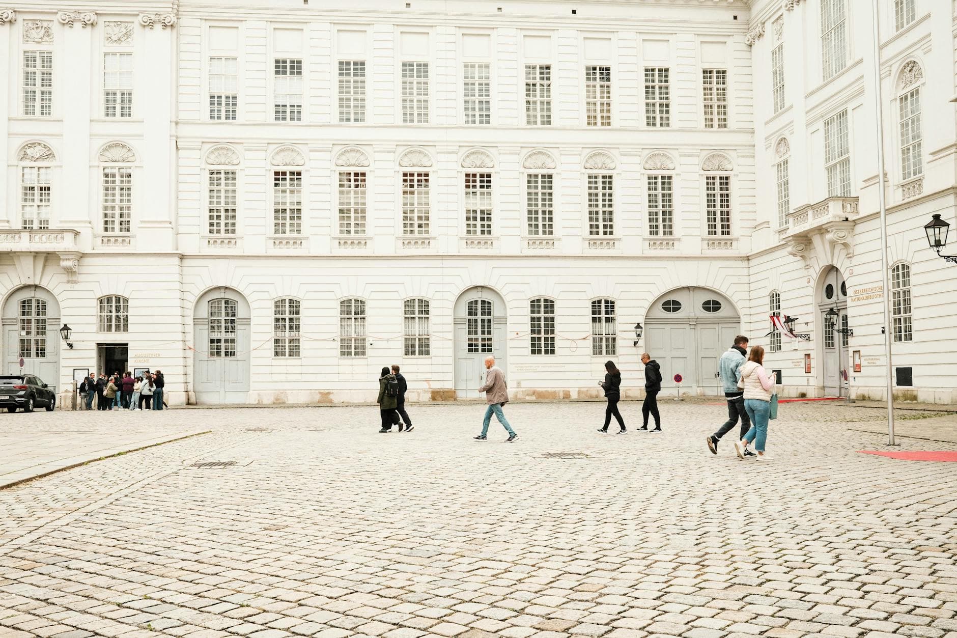 People walking on a cobblestone street by classic white architecture in Vienna.