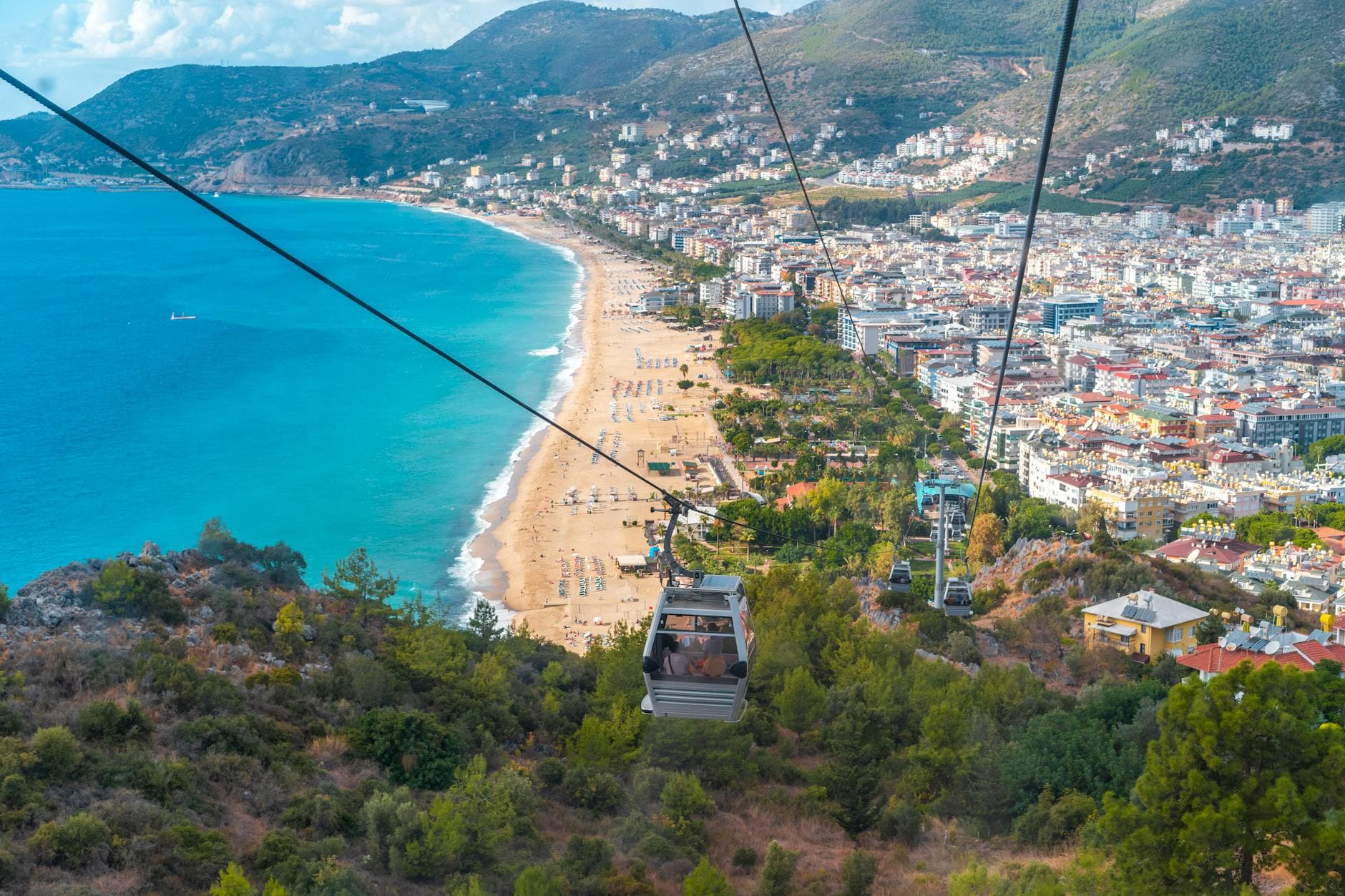 Explore the stunning Alanya coastline and cityscape from a cable car view, capturing beach and mountains.