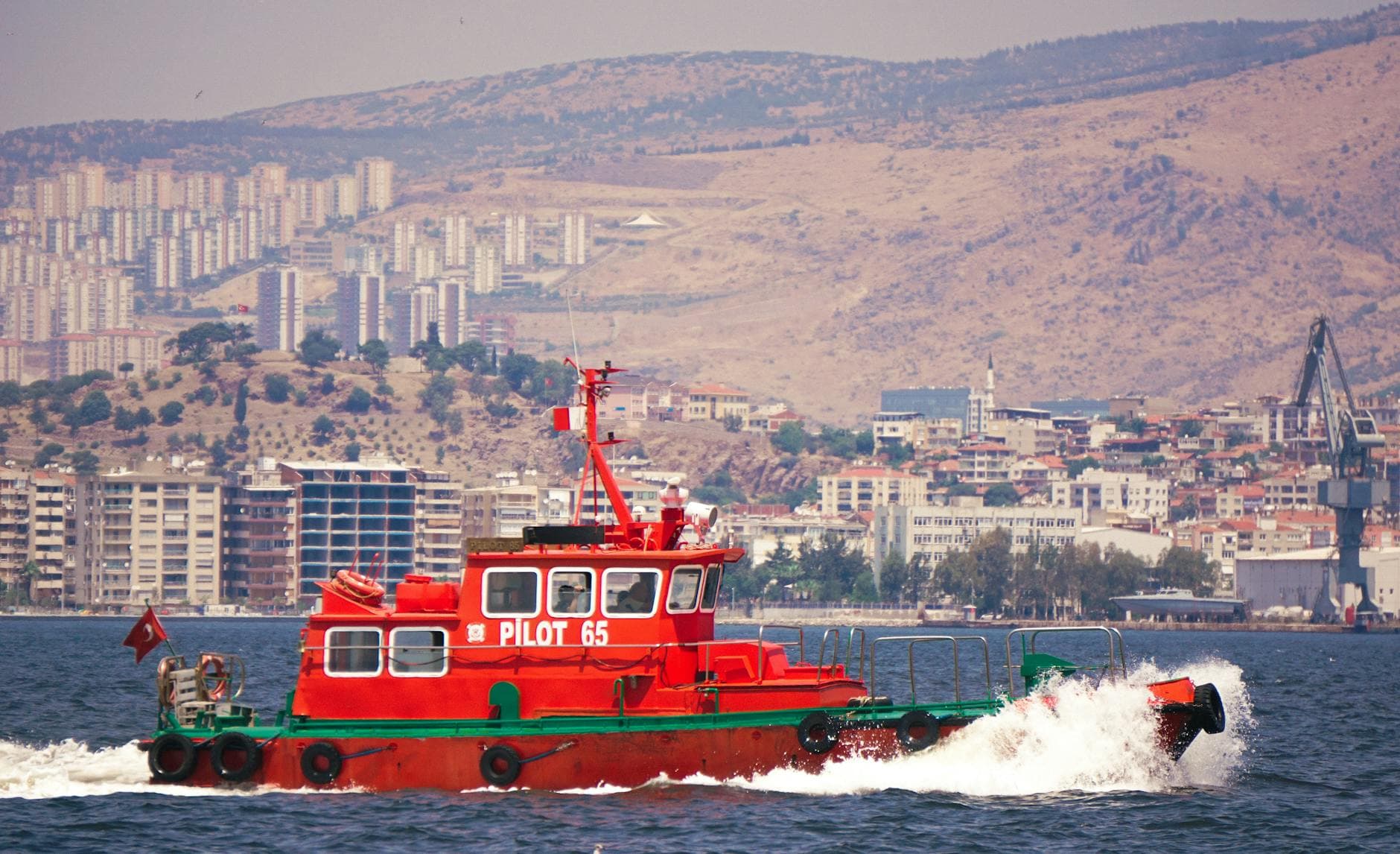 A colorful pilot boat sails in İzmir Bay with a cityscape backdrop in Türkiye.