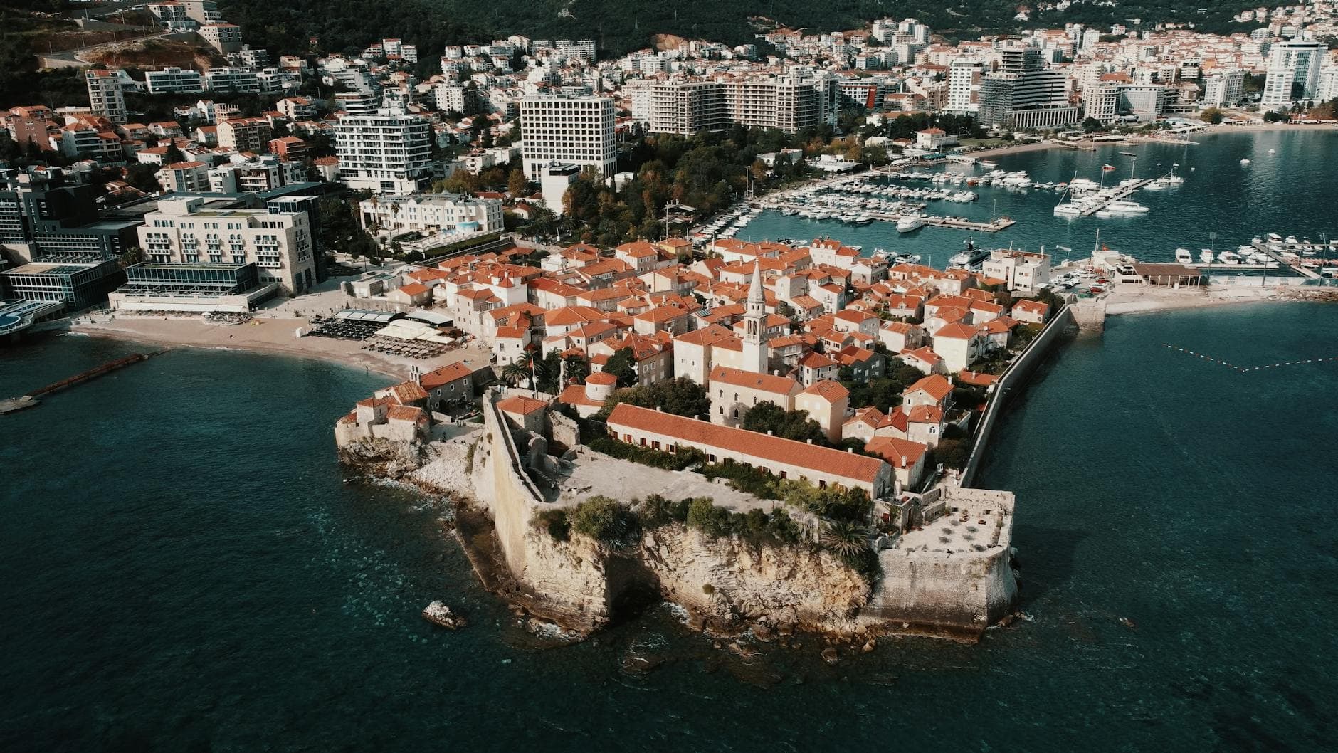 Explore the stunning aerial view of Budva's historic old town with its red-tiled roofs and scenic Adriatic coastline.
