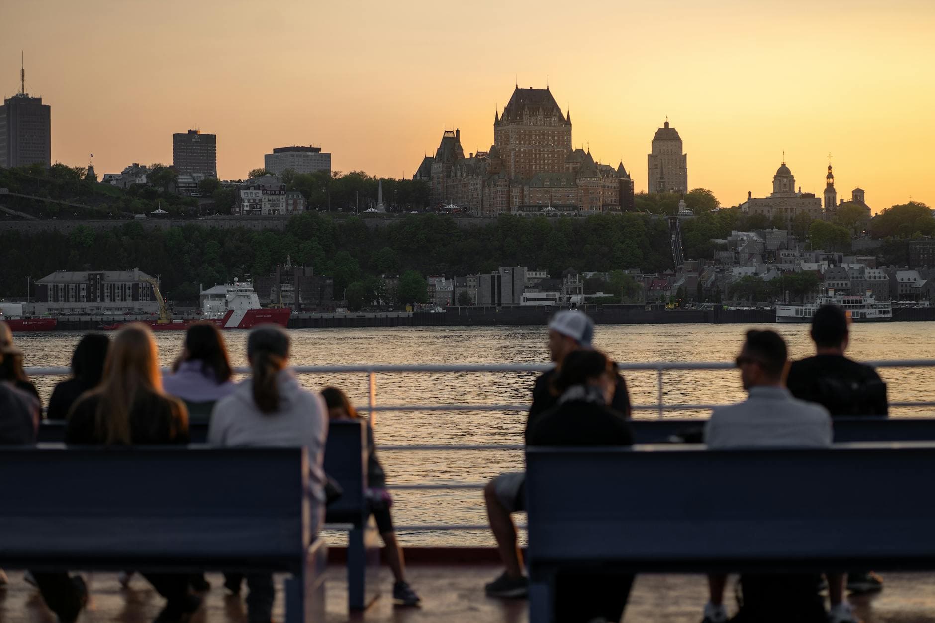 View of Château Frontenac and Quebec City skyline at sunset with people on a waterfront terrace.