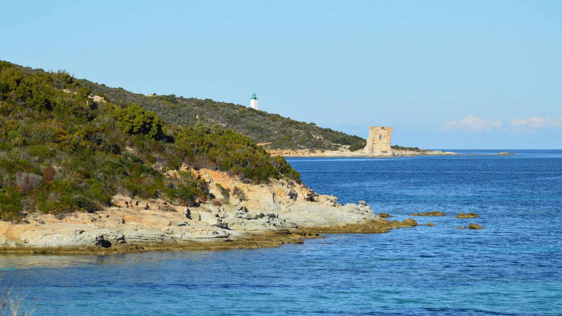 Picturesque landscape of Corsican coastline with rocky shores and a distant lighthouse.