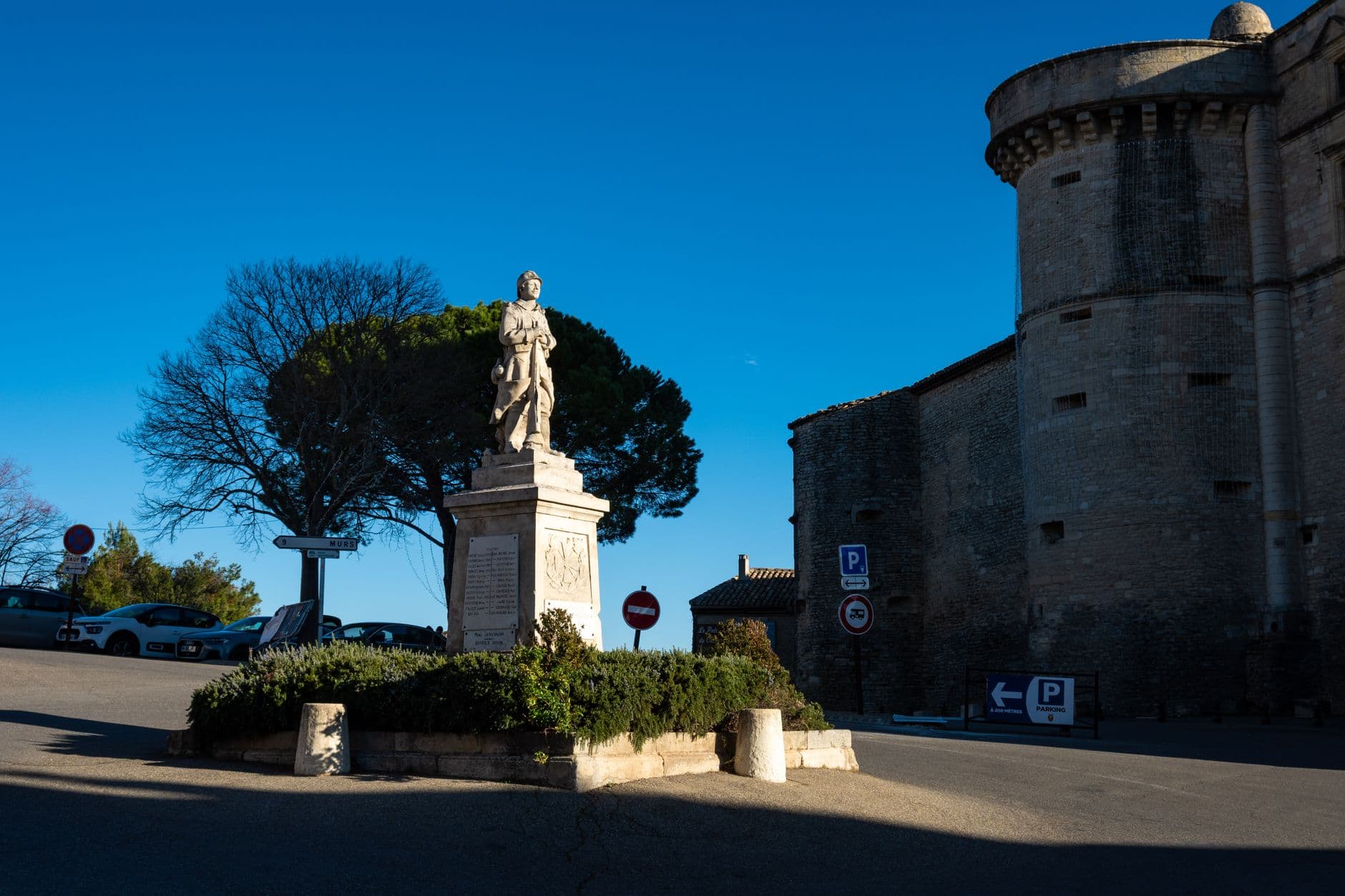 A historic statue and castle exterior in Gordes, Provence, under a clear blue sky.