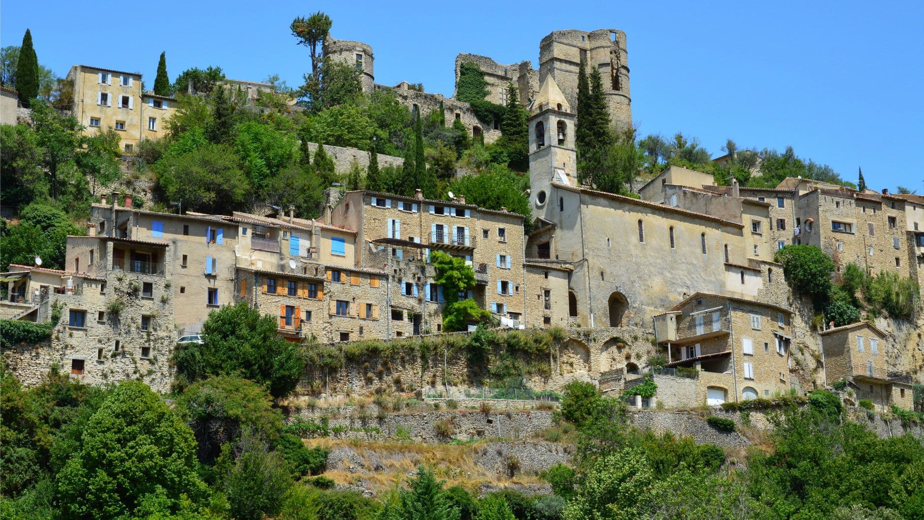 Scenic view of the historic Montbrun-les-Bains village with stone buildings and lush greenery.