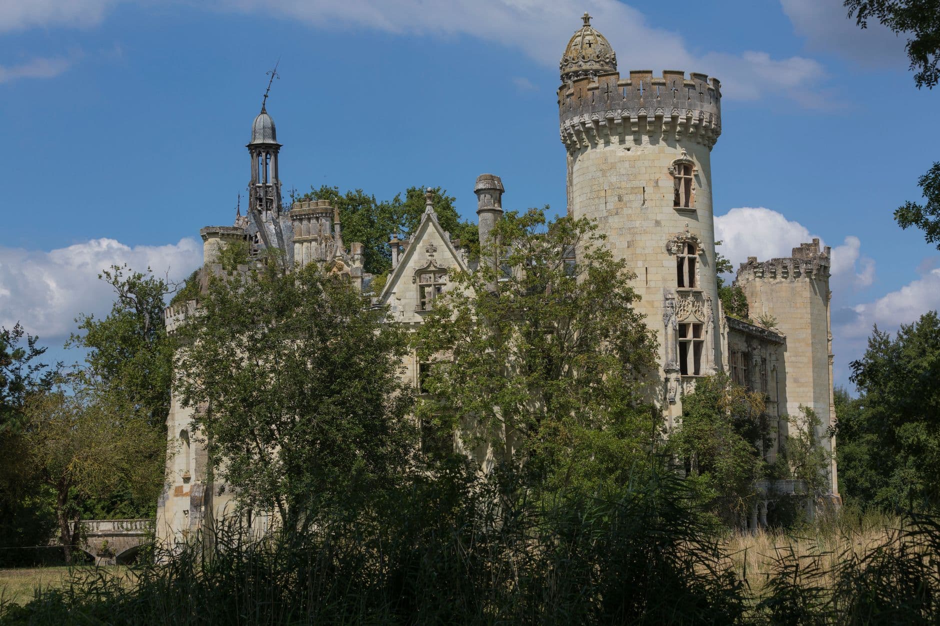 Majestic castle surrounded by trees in Les Trois-Moutiers, France, under a clear sky.