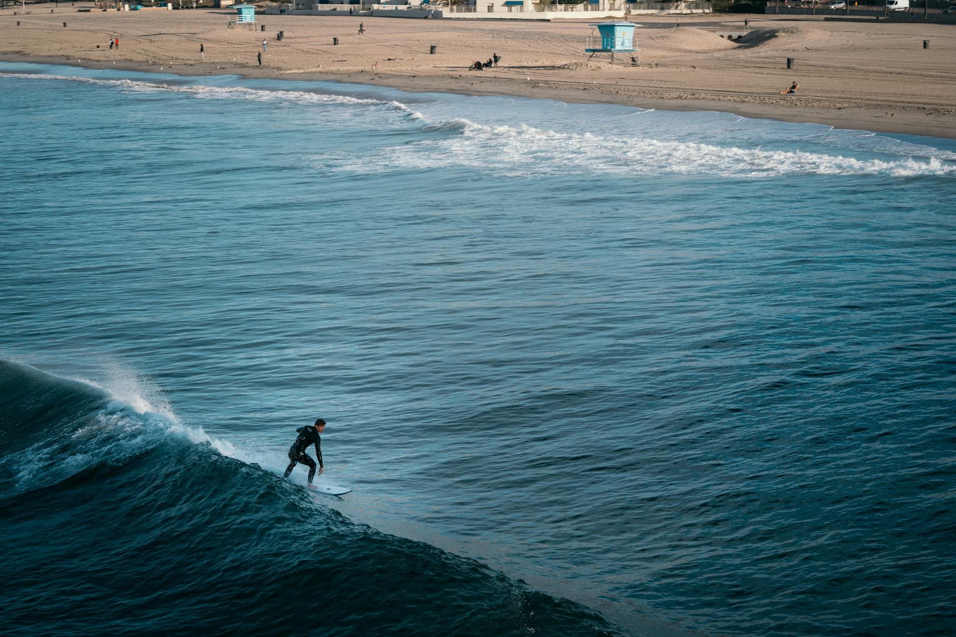 A surfer catching a wave on a sunny day at Malibu Beach with lifeguard towers in view.