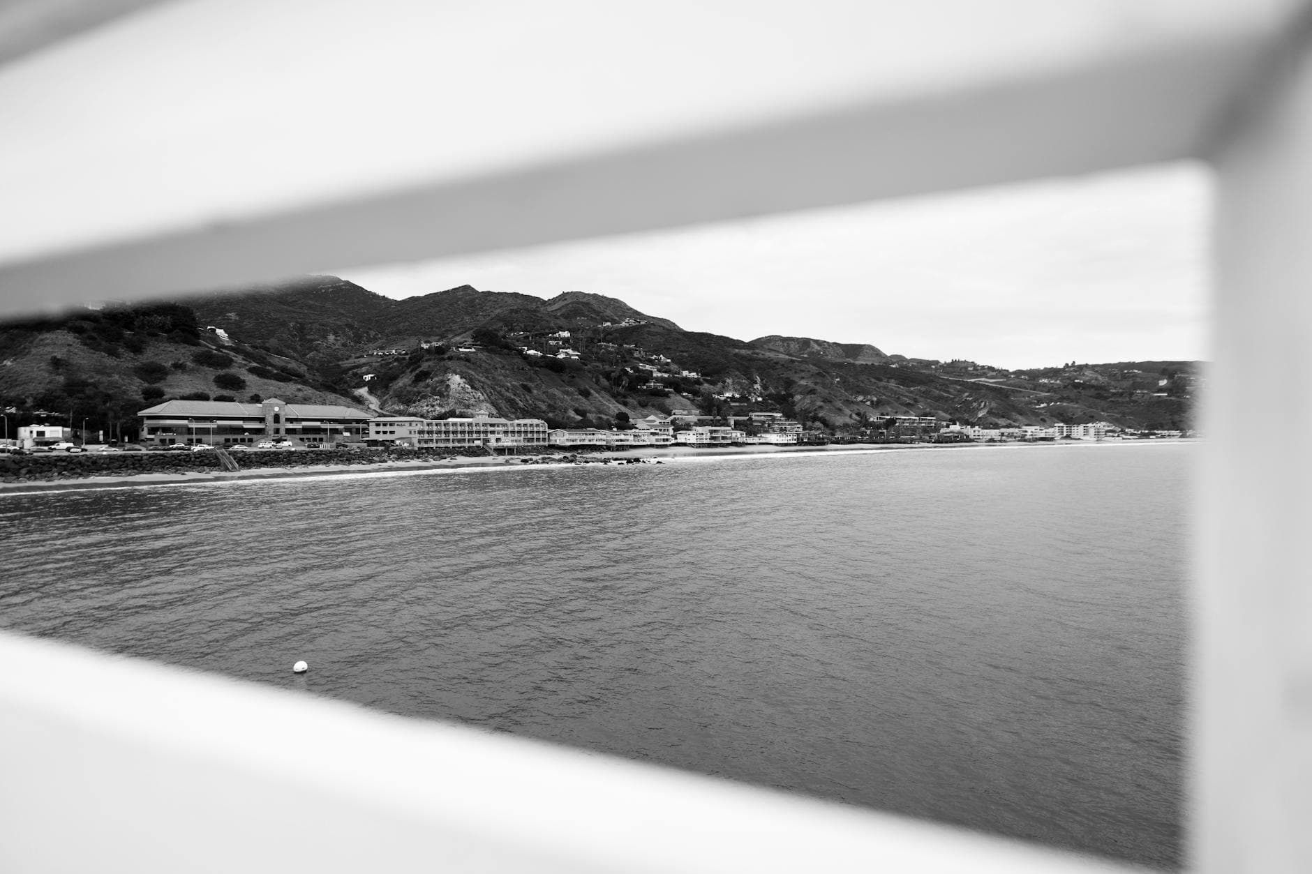 Monochrome view of Malibu's coastline framed by railing, highlighting urban and natural elements.