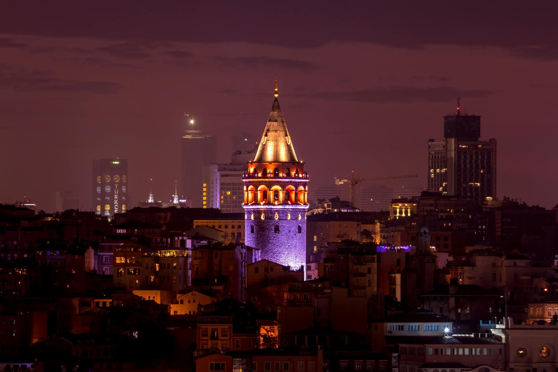 Stunning night view of the iconic Galata Tower in Istanbul, surrounded by city lights and skyscrapers.