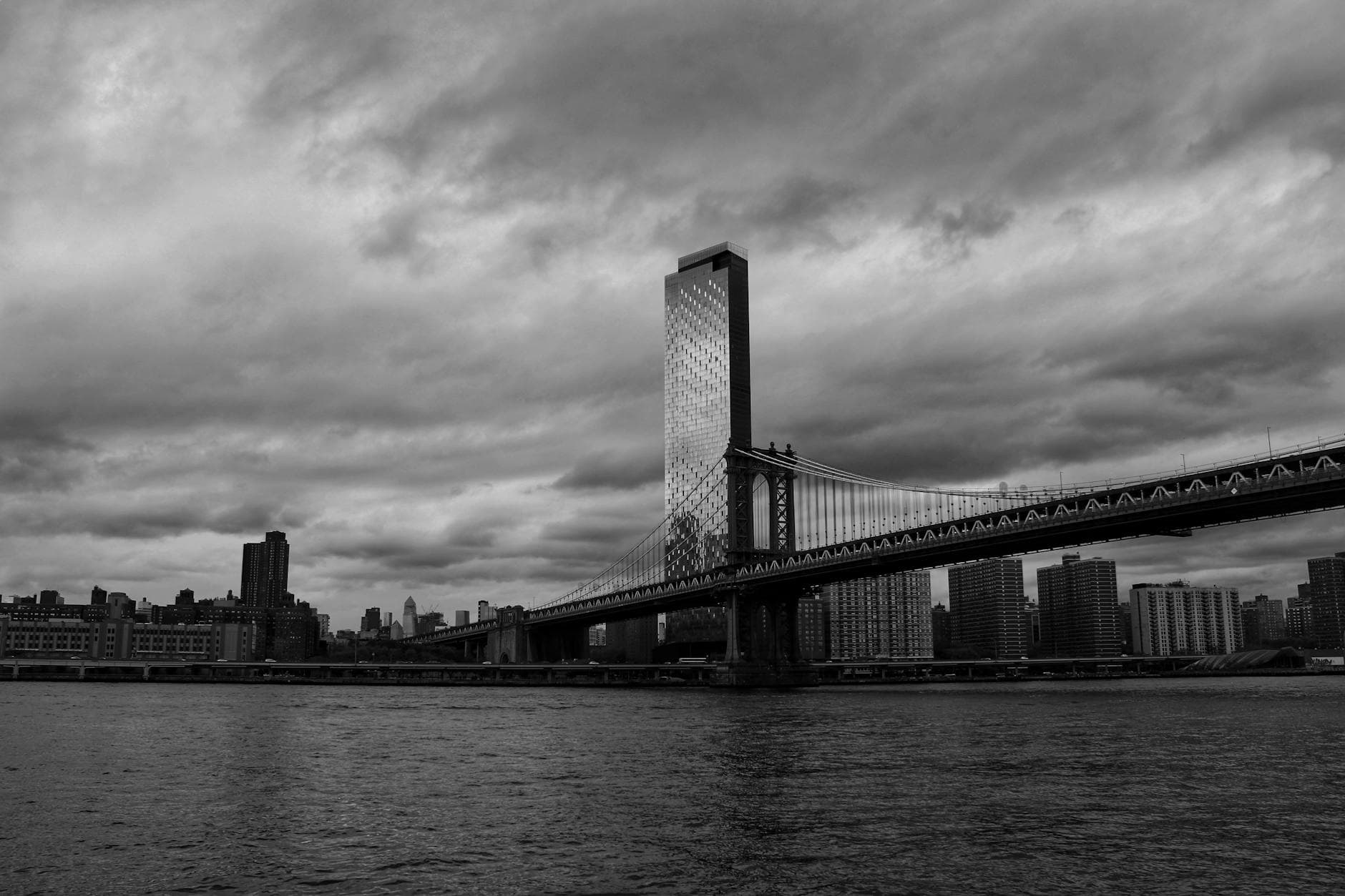 Dramatic skyline featuring the Manhattan Bridge and New York City in black and white, showcasing urban architecture.