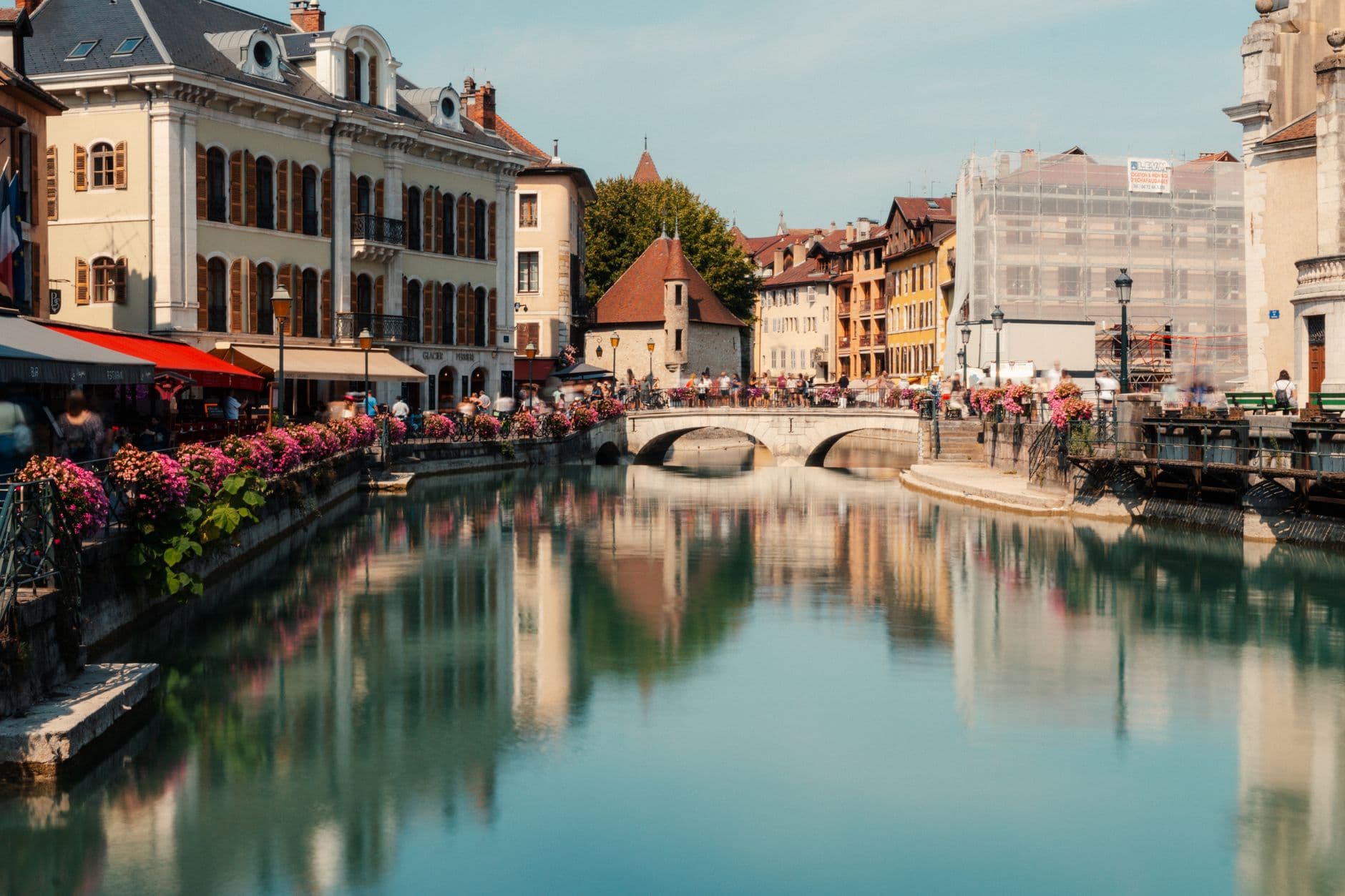 Picturesque canal scene in Annecy, France with historic buildings and a scenic bridge reflecting in the water.