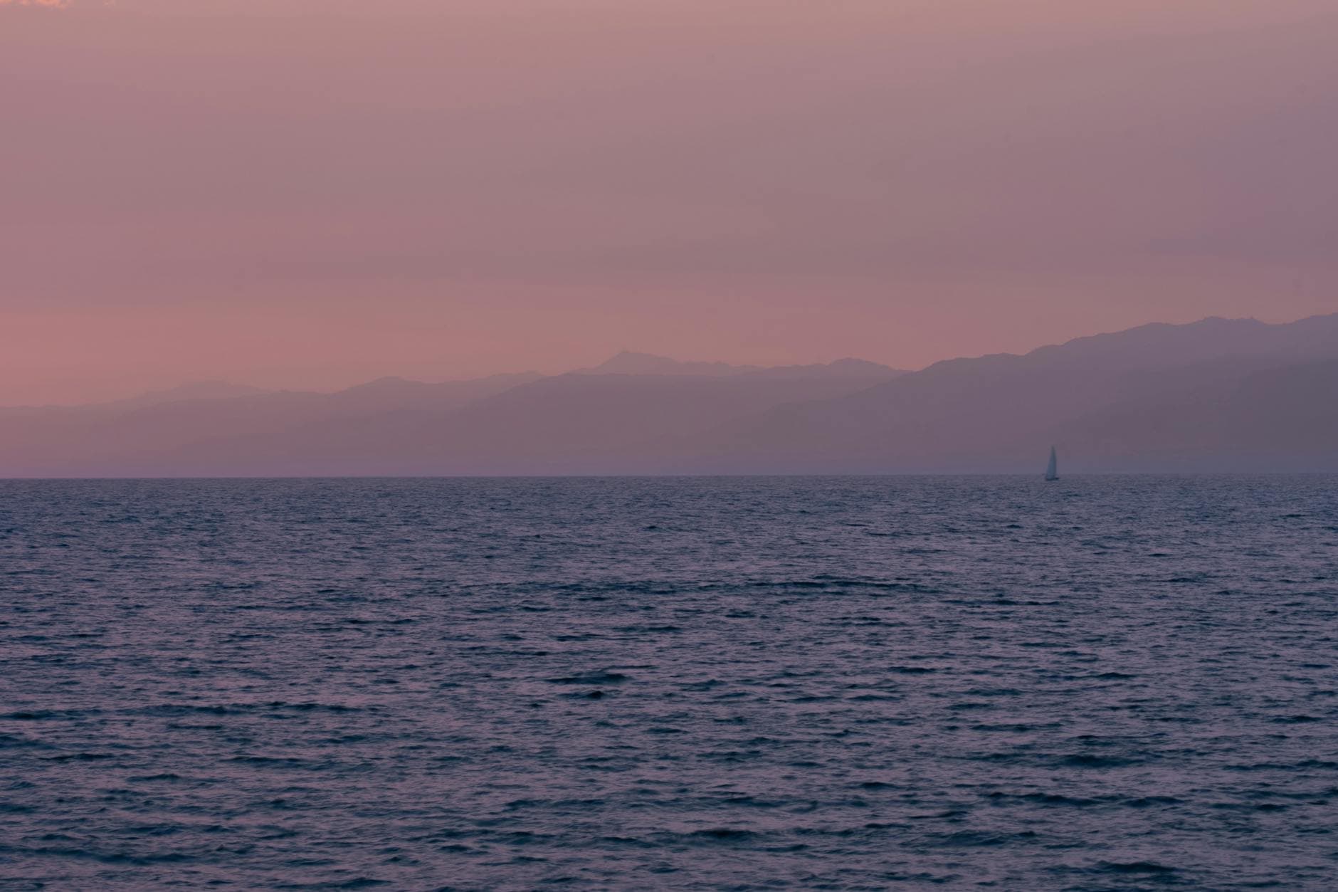 A serene sunset view over the ocean in Marina del Rey, California with subtle pink hues and a distant sailboat.