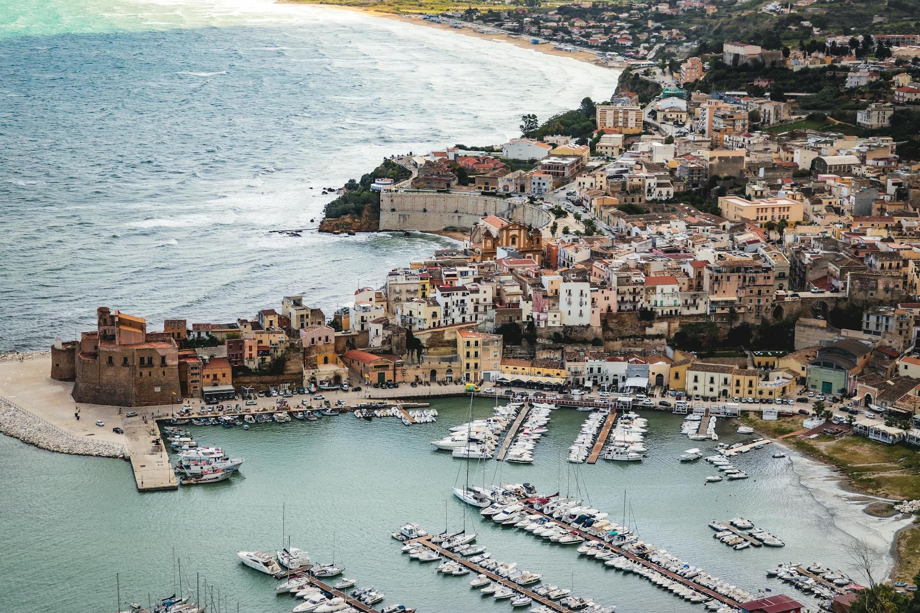 A picturesque aerial shot of a coastal town in Sicily, showcasing the marina and historic architecture.