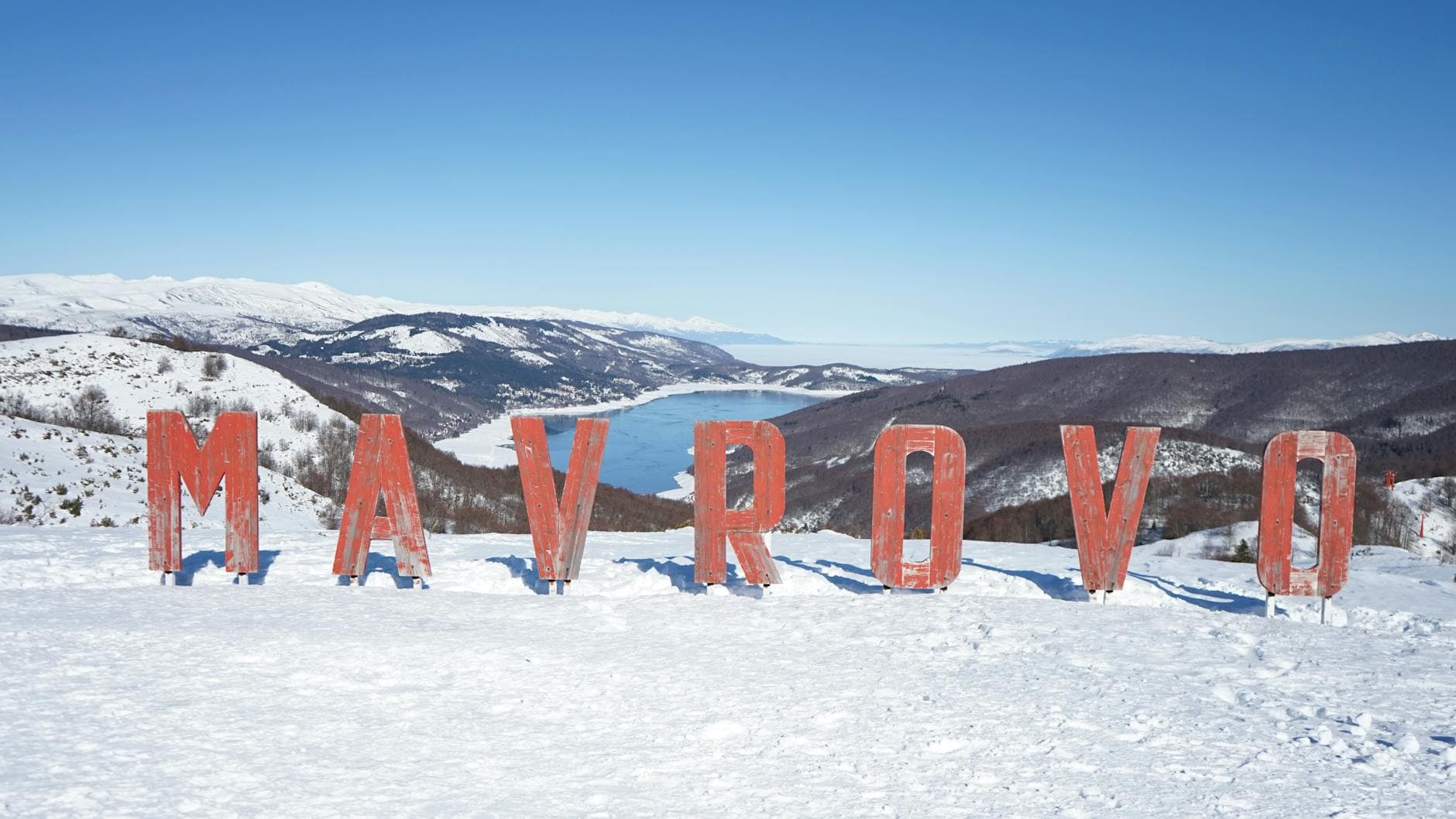 Scenic winter landscape of Mavrovo with snowcapped mountains and lake.