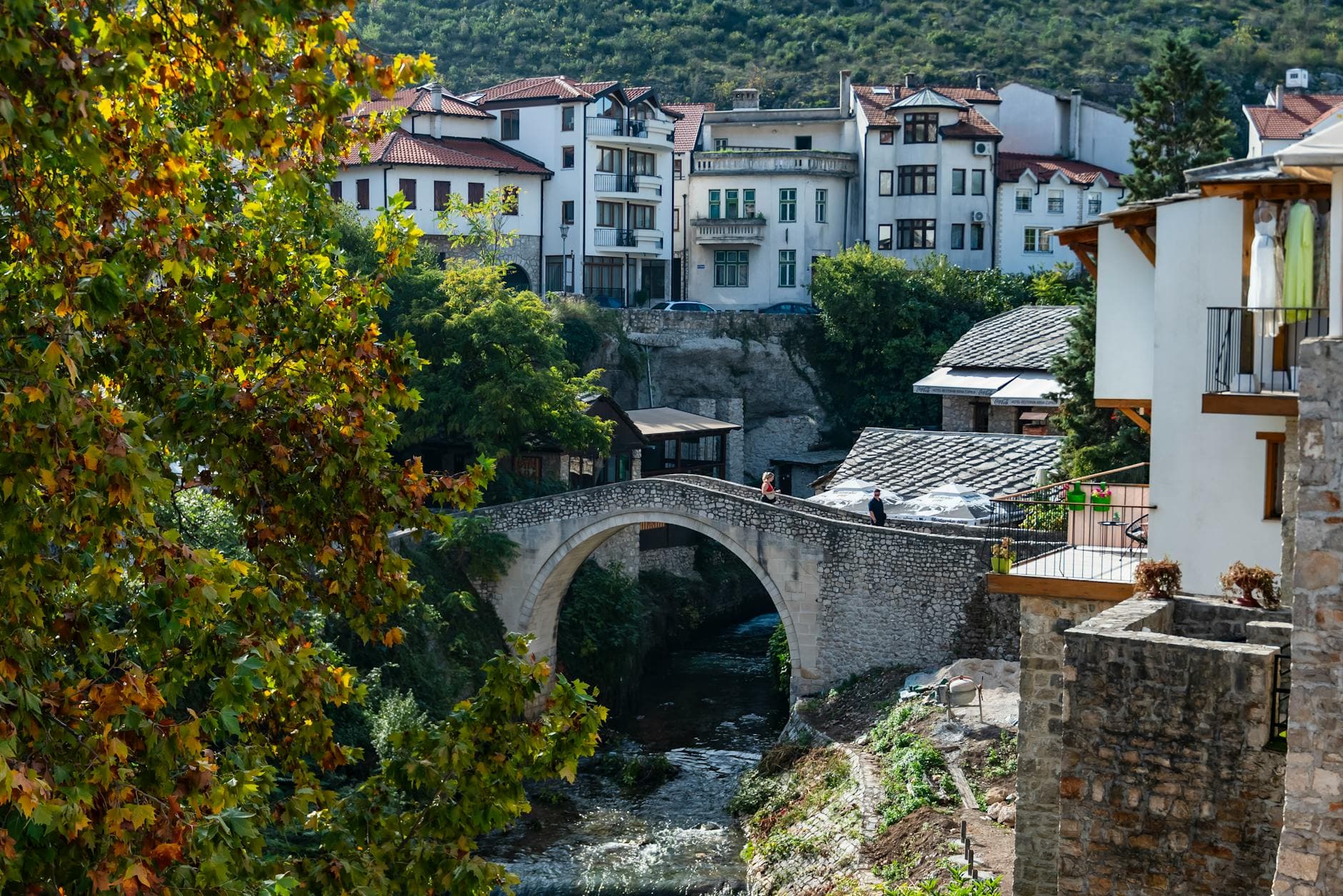 Scenic view of a historic stone bridge in Mostar with trees and houses in the background.
