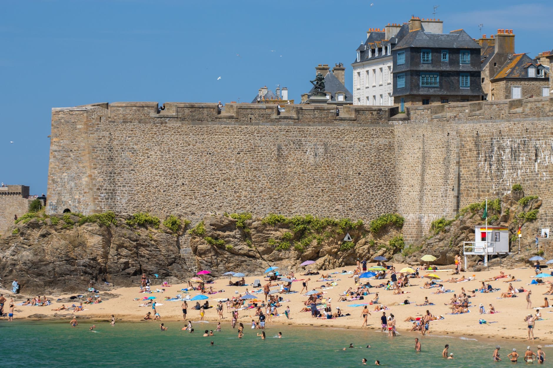 Beachgoers enjoy a sunny day by the historical city walls of Saint-Malo, France.