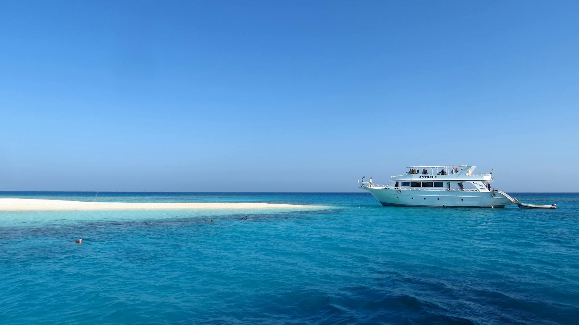 A scenic view of a luxury yacht by a pristine, sandy island in Egypt's vibrant blue waters.