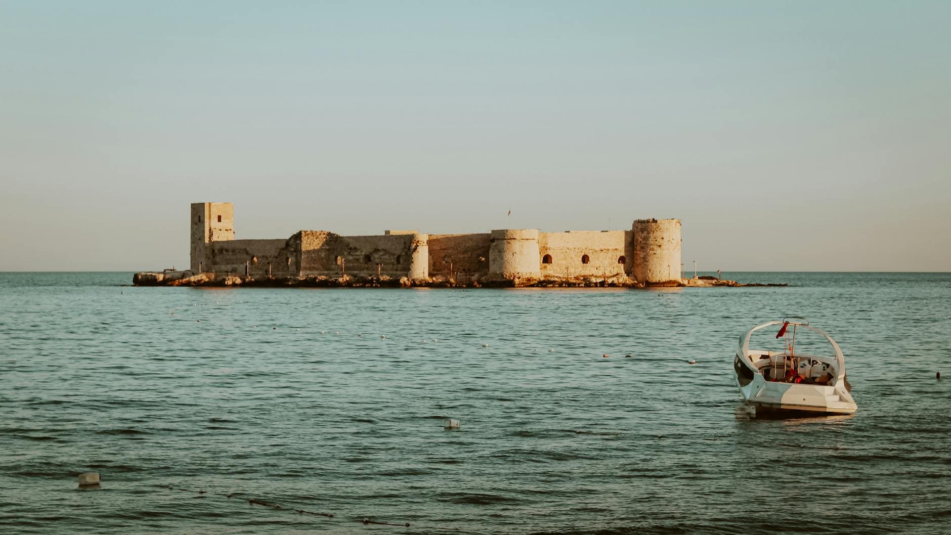 Scenic view of Kizkalesi Castle in Mersin, Turkey with a small boat on a tranquil sea under a clear sky.