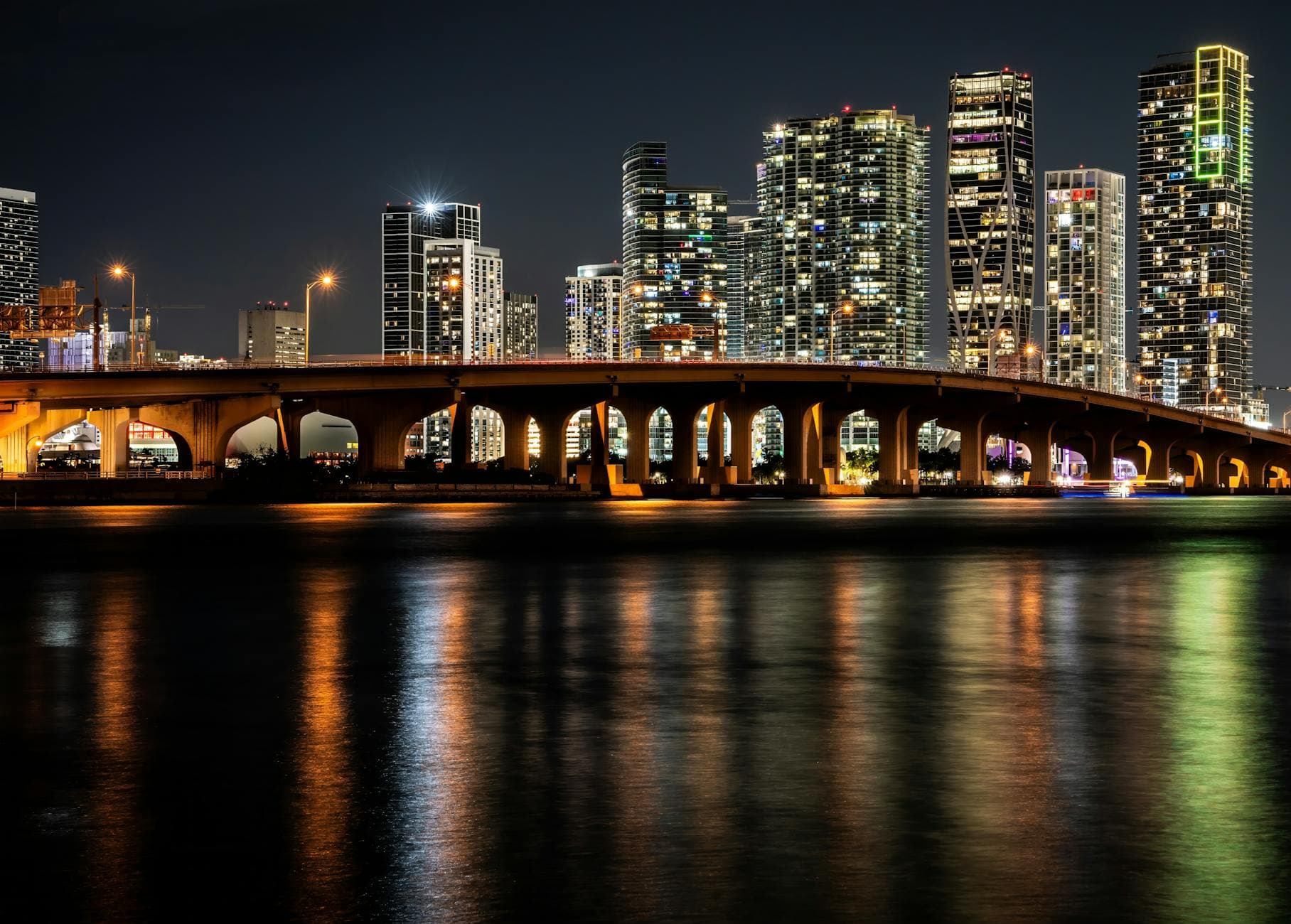 Gorgeous night view of Miami's illuminated skyline and bridge reflections on water, offering a captivating cityscape.