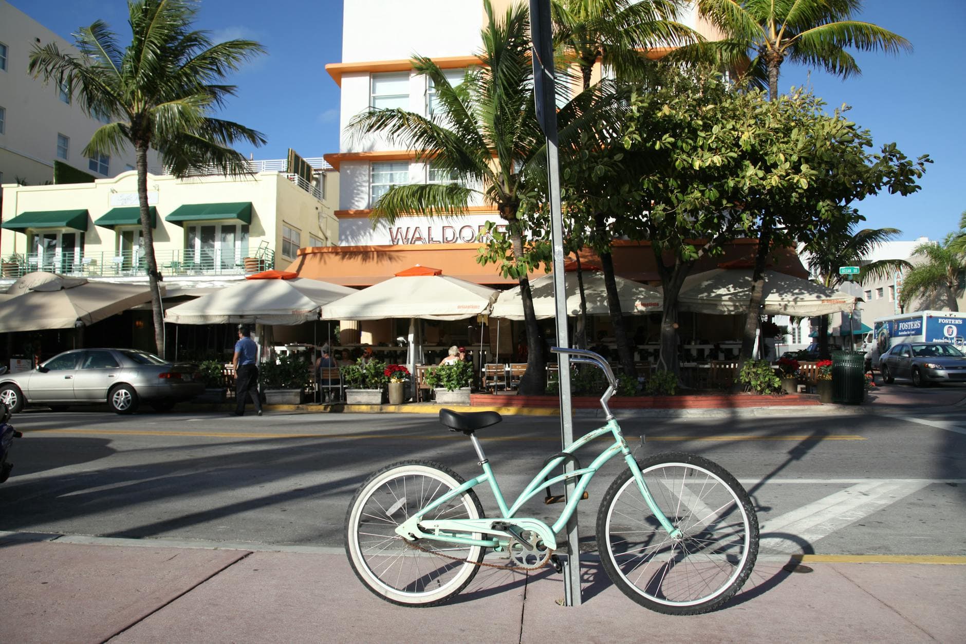 A bicycle is parked on a sunny Miami Beach street with palm trees and art deco architecture in the background.