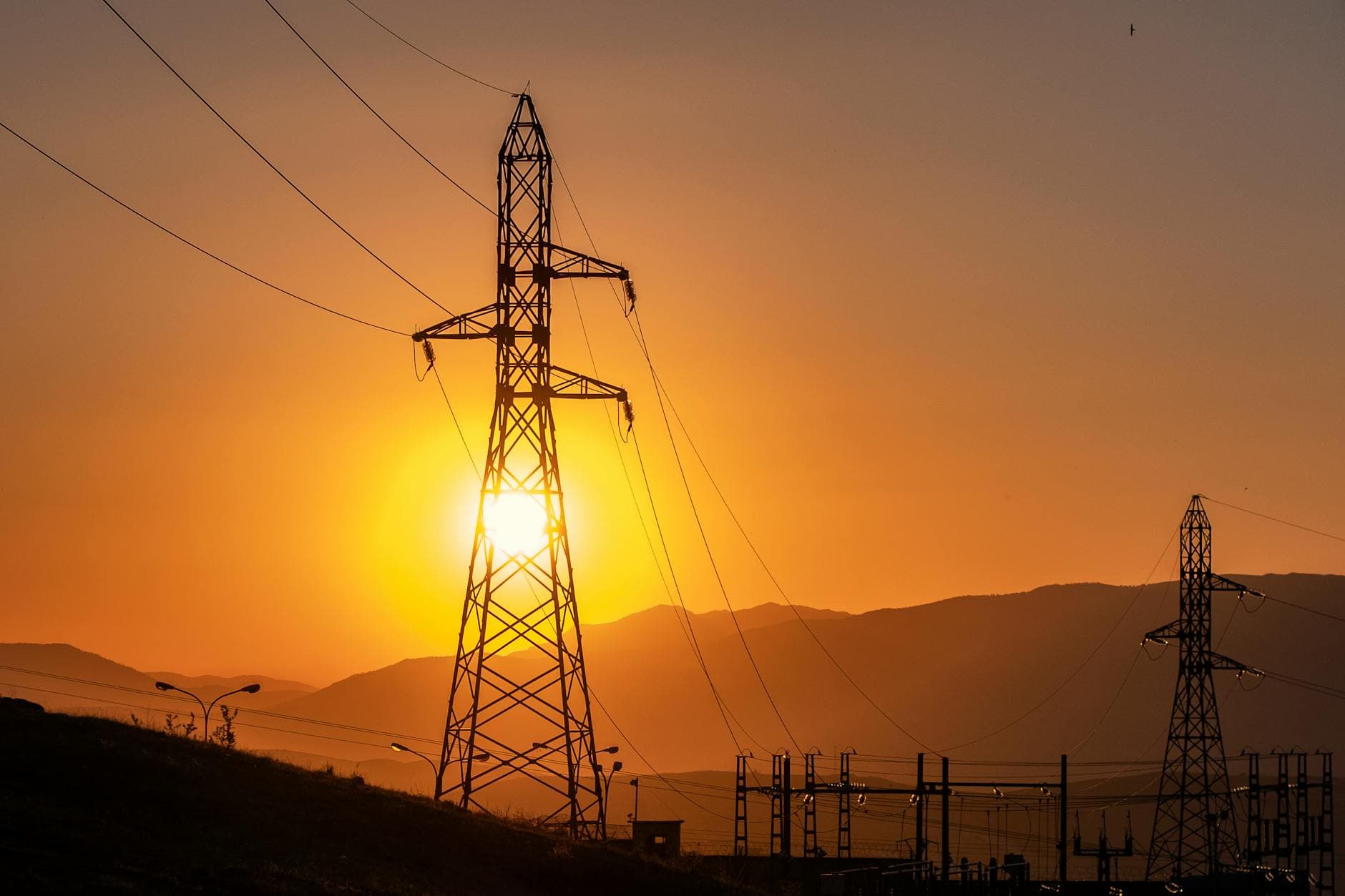 A striking view of an electrical tower silhouetted against a vibrant sunset in Mila, Algeria.