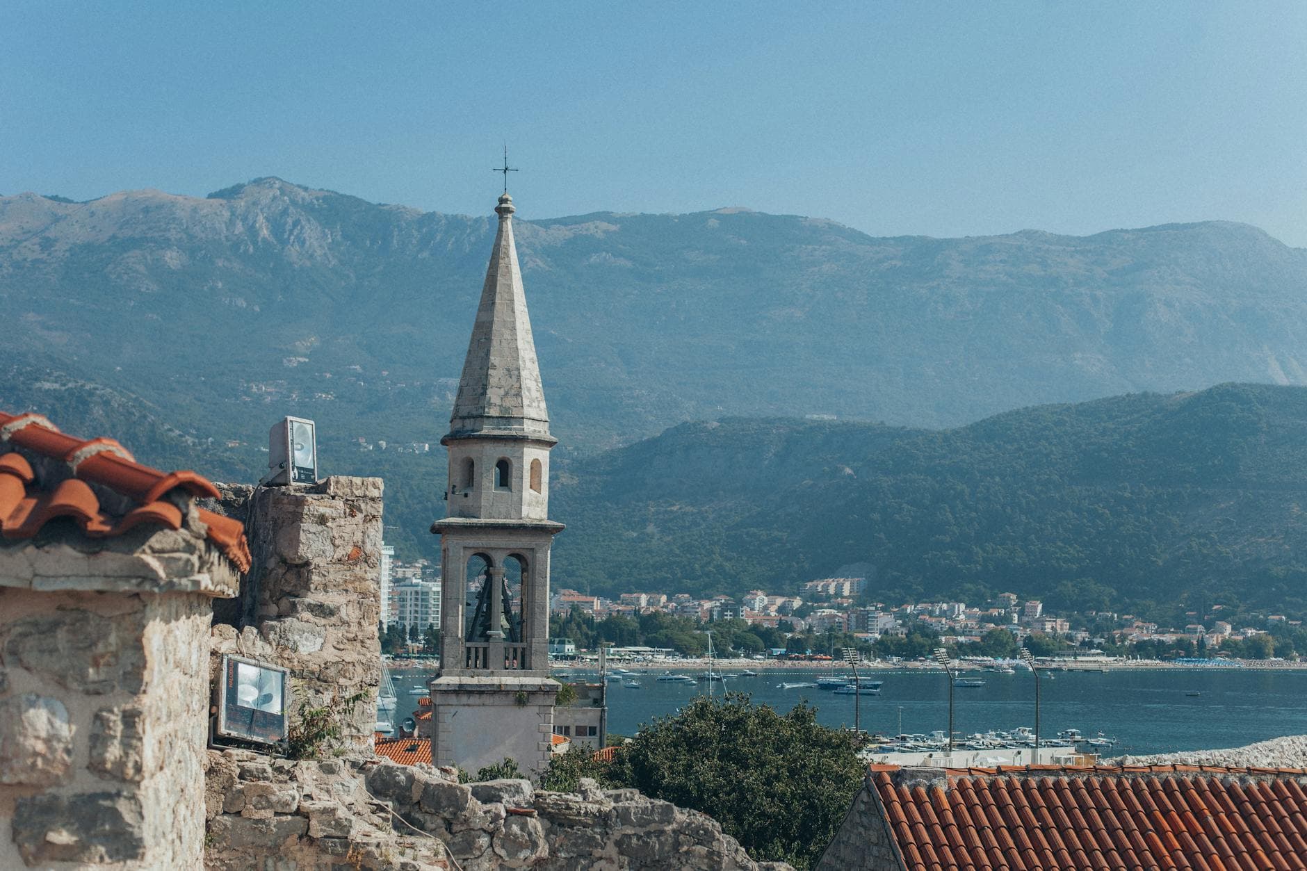 A scenic view of a church tower and coastline in Montenegro with mountains in the background.