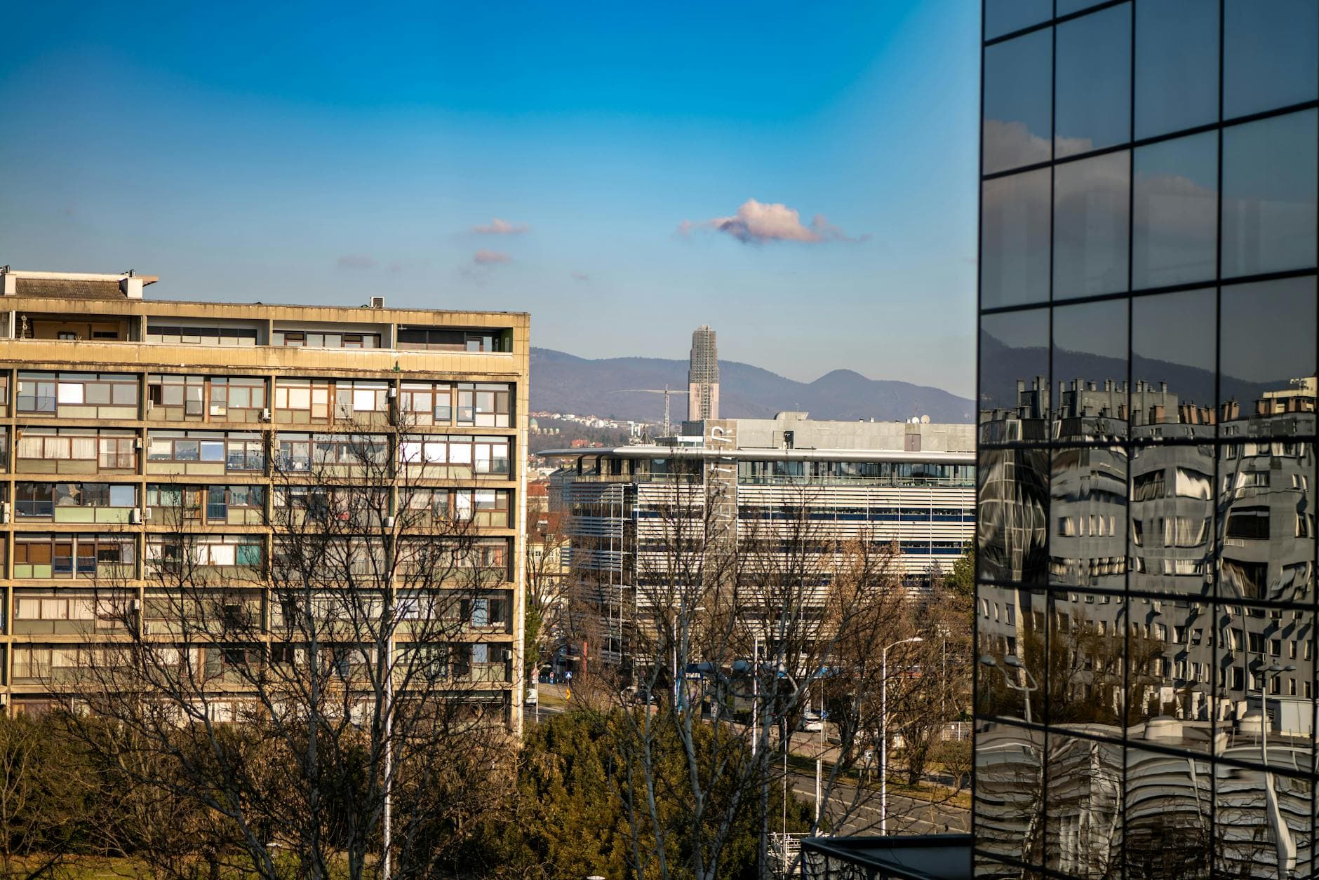 Urban skyline of Zagreb with glass reflections and mountains in the backdrop.