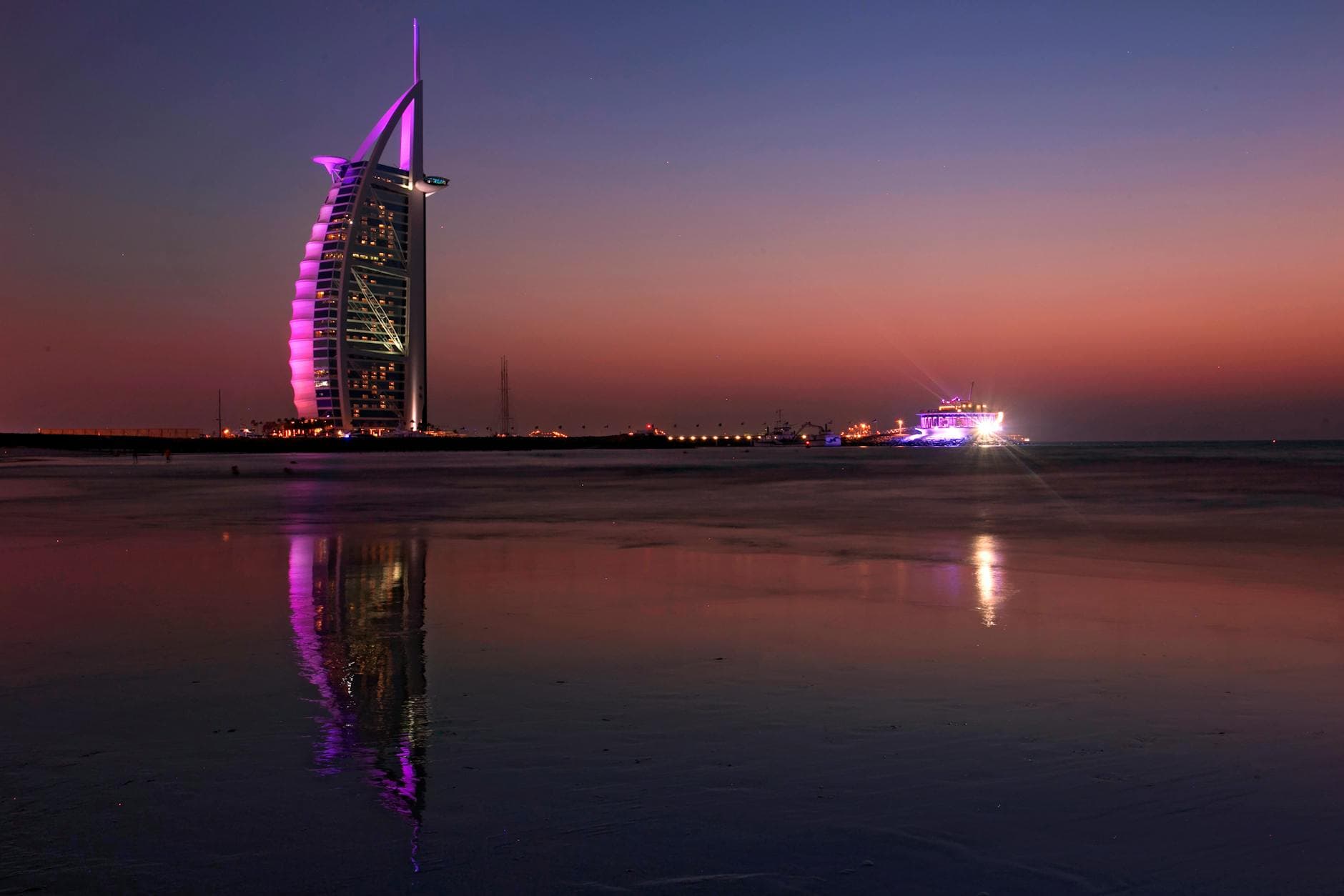 Burj Al Arab illuminated at twilight reflecting on the beach in Dubai, UAE.