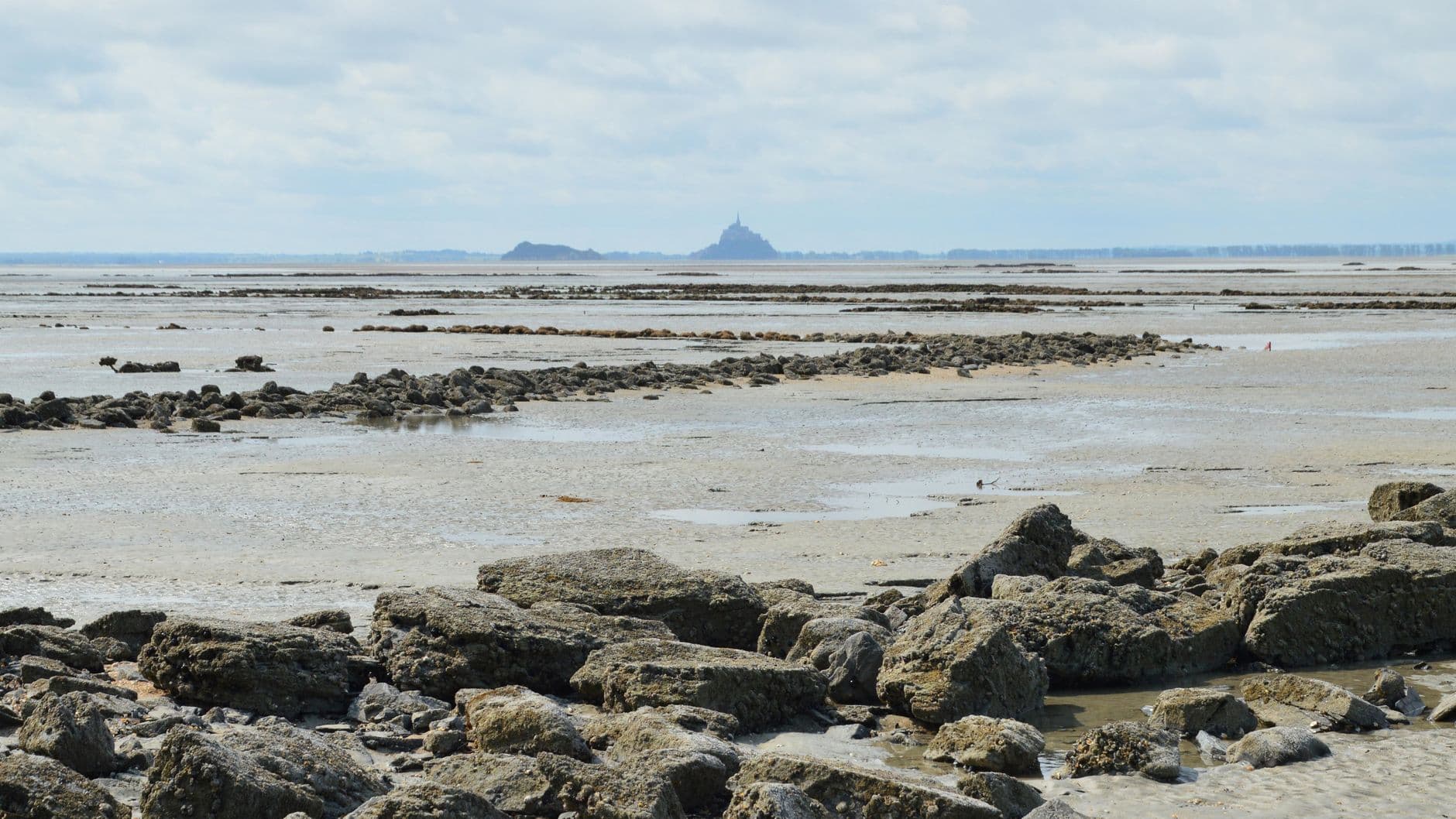 Scenic view of the rocky shoreline in Saint-Jean-le-Thomas, Normandie, France with distant view of Mont Saint-Michel.