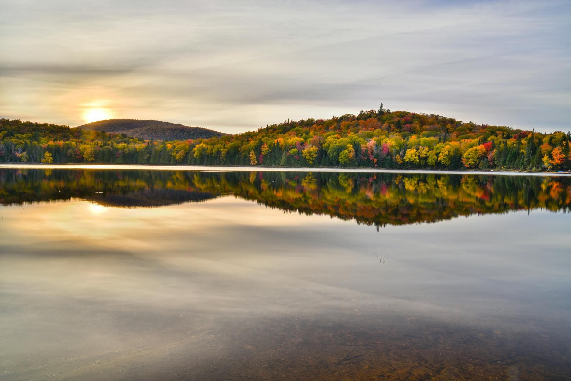 Stunning autumn view of Mont-Tremblant's colorful forests reflected in the calm lake at sunset.