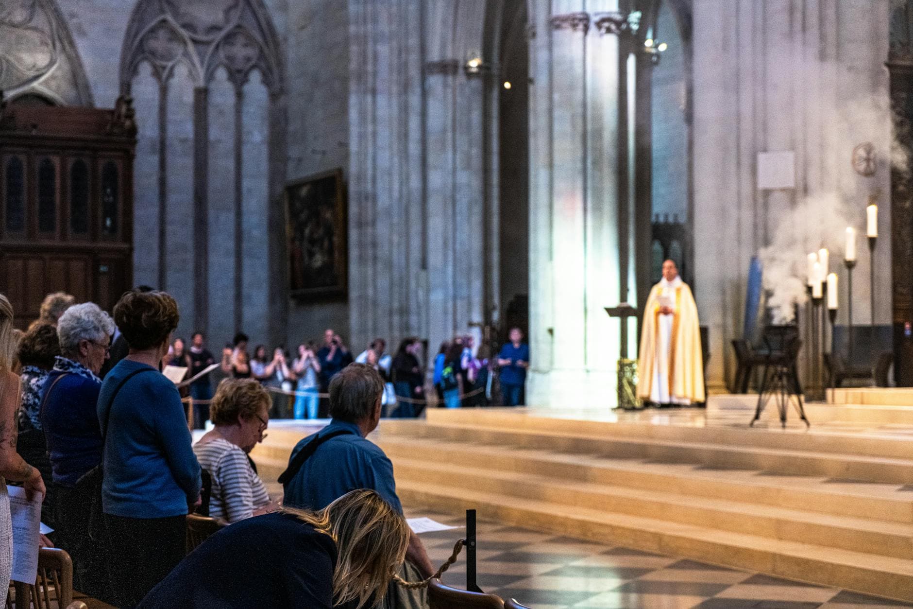 Congregation during a mass in a historic Paris cathedral with lit candles and smoke.