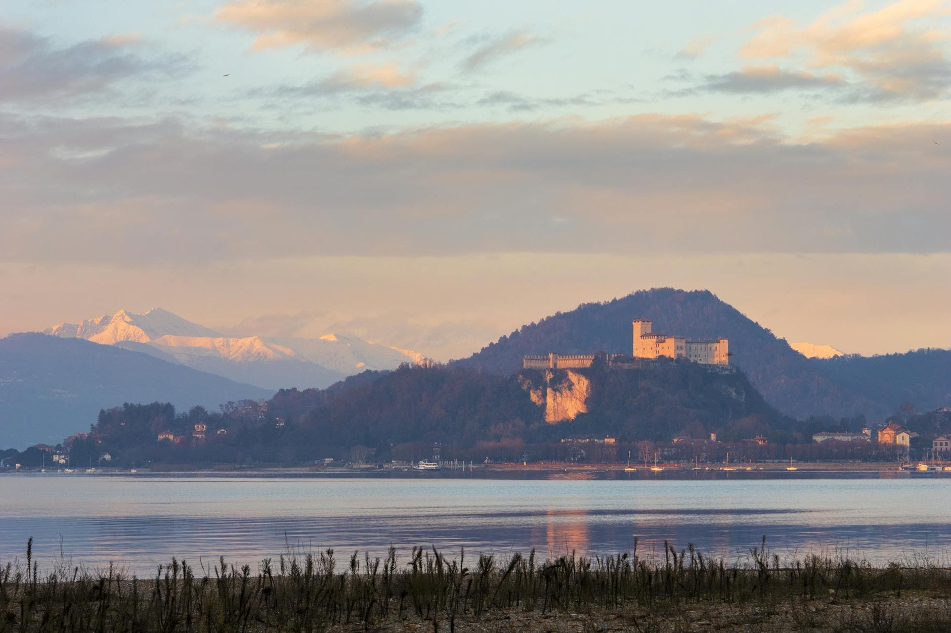 Scenic landscape of a historic castle on a hill with mountains in the background during sunset.